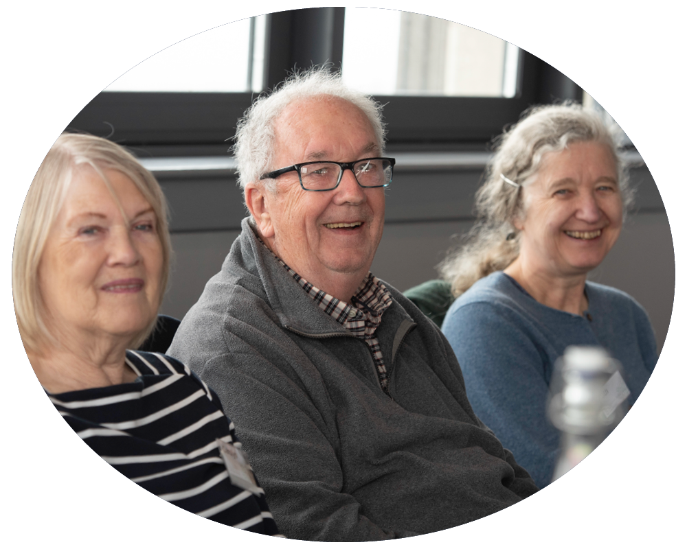 Three senior adults sitting and smiling in a brightly lit room.