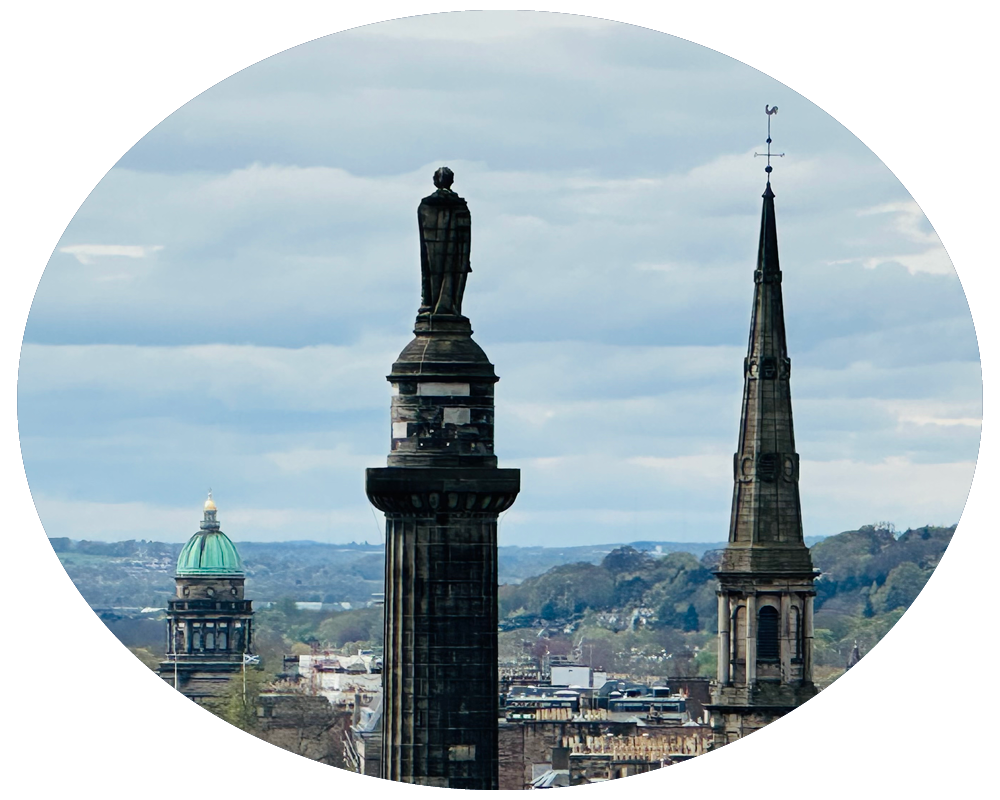 View of city skyline with church steeples and a statue on a tall pedestal under cloudy sky.