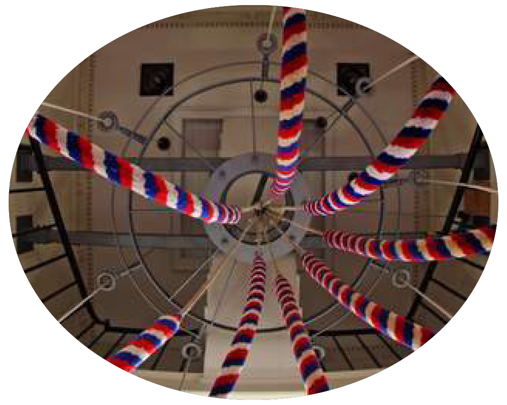 A view of six barber poles with red, white, and blue stripes, arranged in a circular pattern from below, with a ceiling and walls of a building in the background.