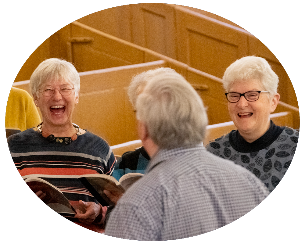 Four older adults laughing and talking in a church or community hall with wood paneling in the background.