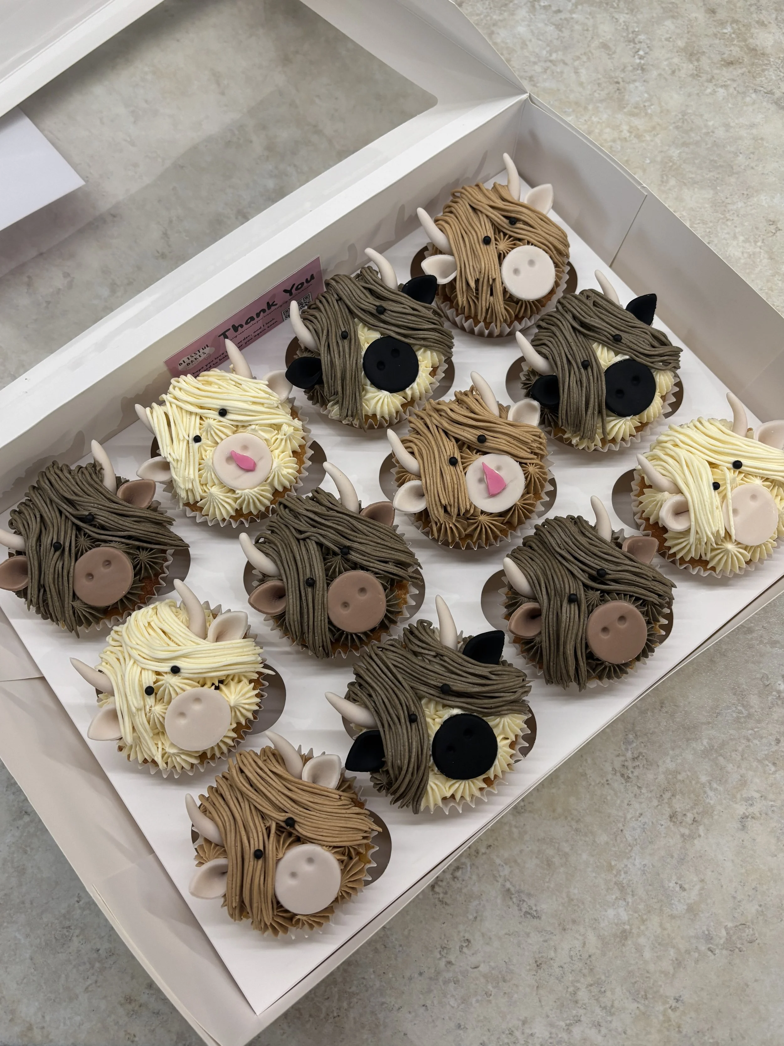 A box of cupcakes decorated as wild boars with fondant horns, ears, and eyes, and piped hair to resemble wild boars.