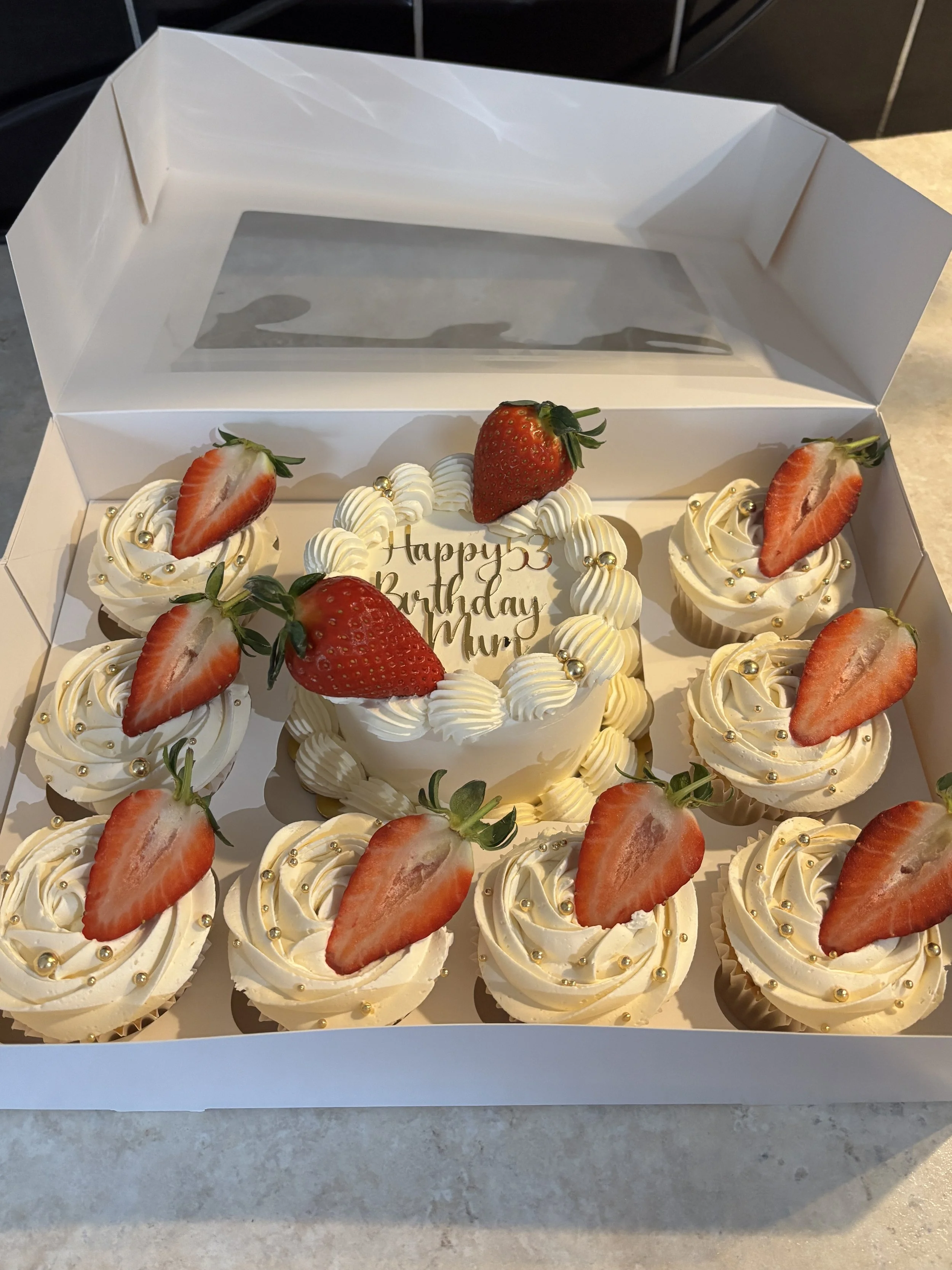 A birthday cake and cupcakes decorated with strawberries and gold-colored beads, with a message that reads "Happy 53 Birthday Mum" in the cake topper.