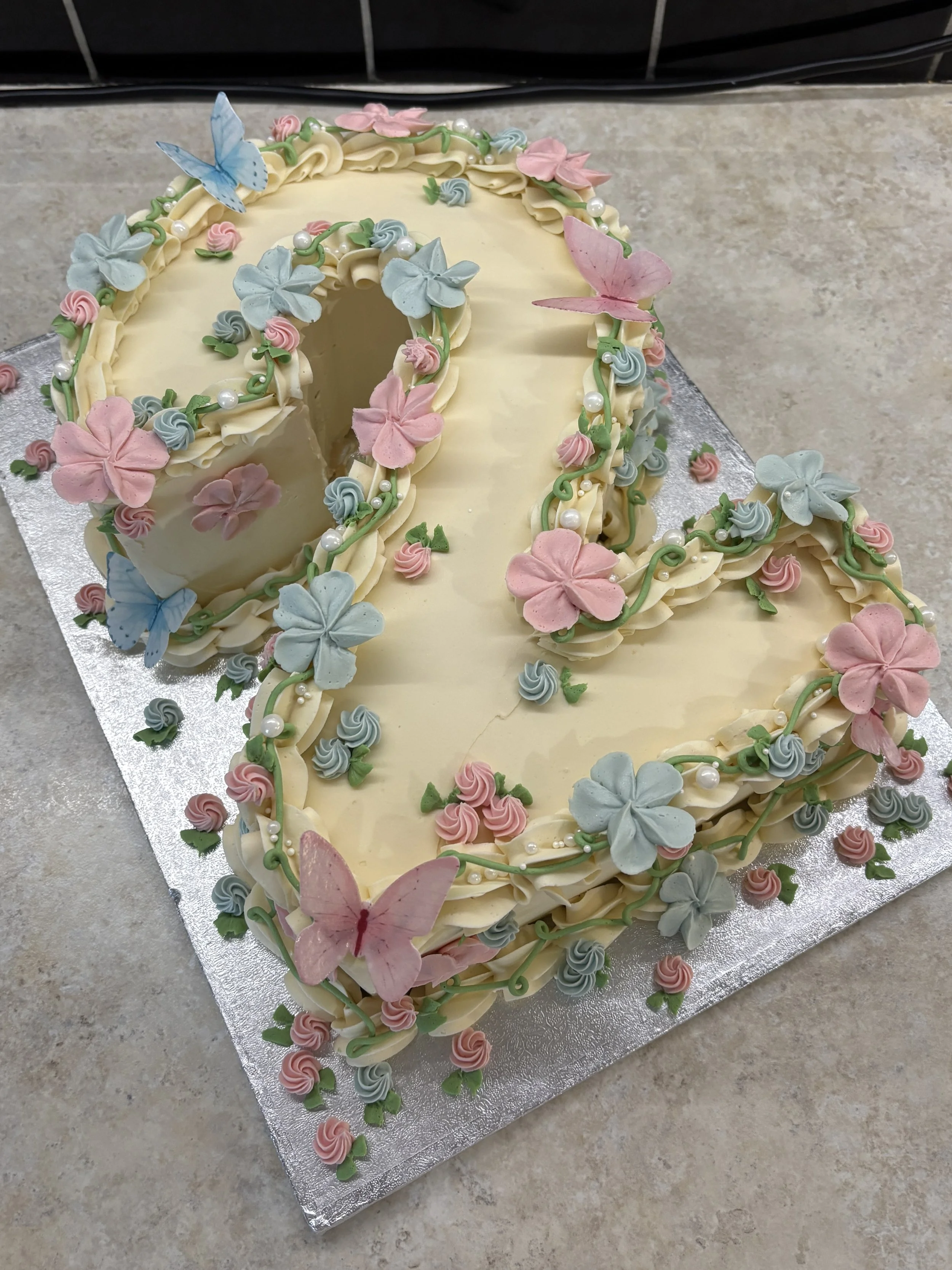 A large, heart-shaped cake decorated with pastel pink and blue flowers, green leaves, and edible pearls.