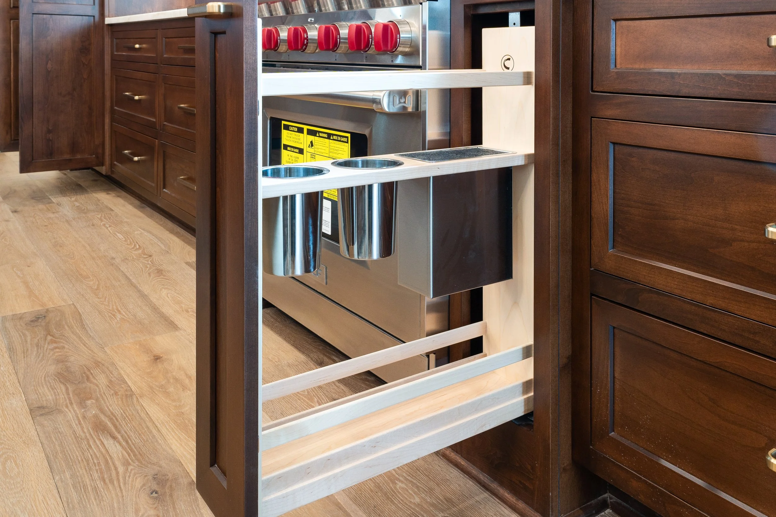 Empty kitchen cabinet frame with wood finish, showing the inside with wood shelves and a built-in stove with red knobs.