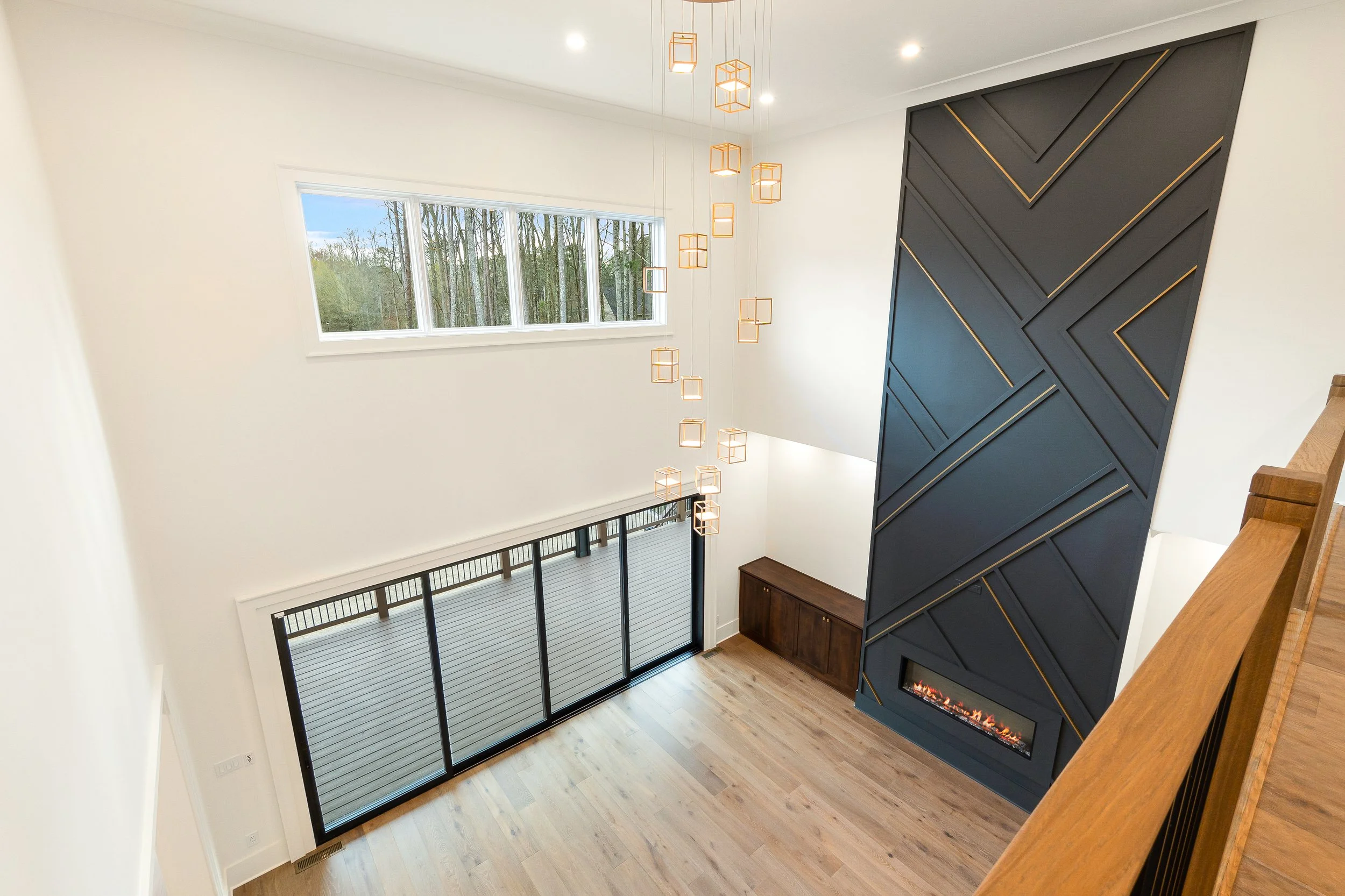 Modern living room with large window, hanging geometric light fixtures, and a blue accent wall with a built-in fireplace.