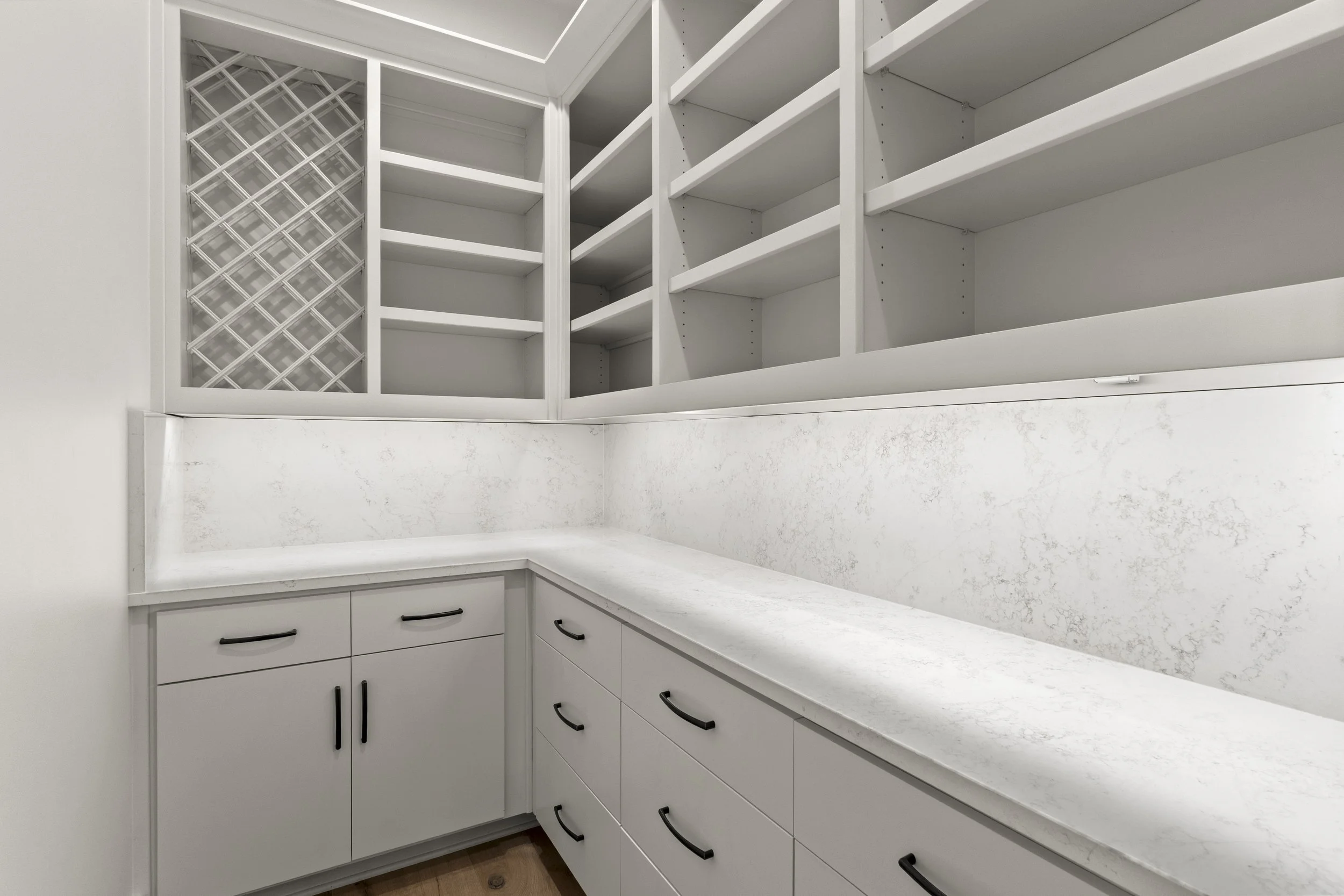 Kitchen corner with white cabinets, black handles, white marble countertop, and open white shelving above, with a wine rack on the left side.