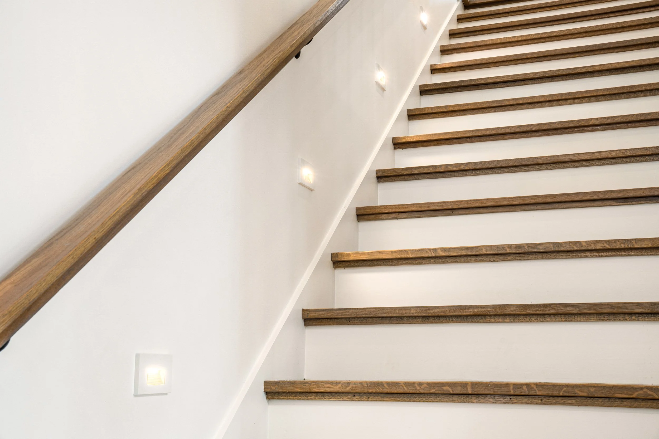 Wooden staircase with white walls and small wall-mounted lights.
