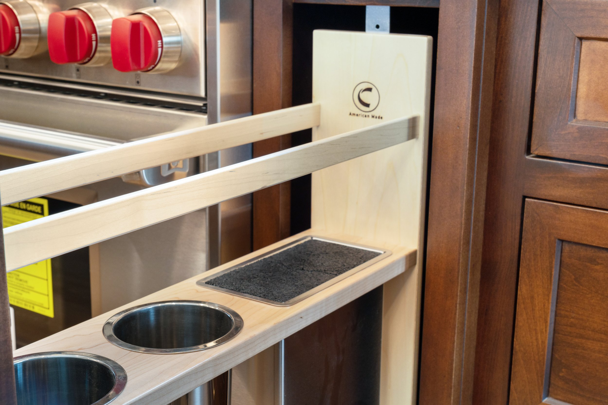 Empty wooden pet feeding station with two metal bowls and a black textured tray, set against a dark wood cabinet.