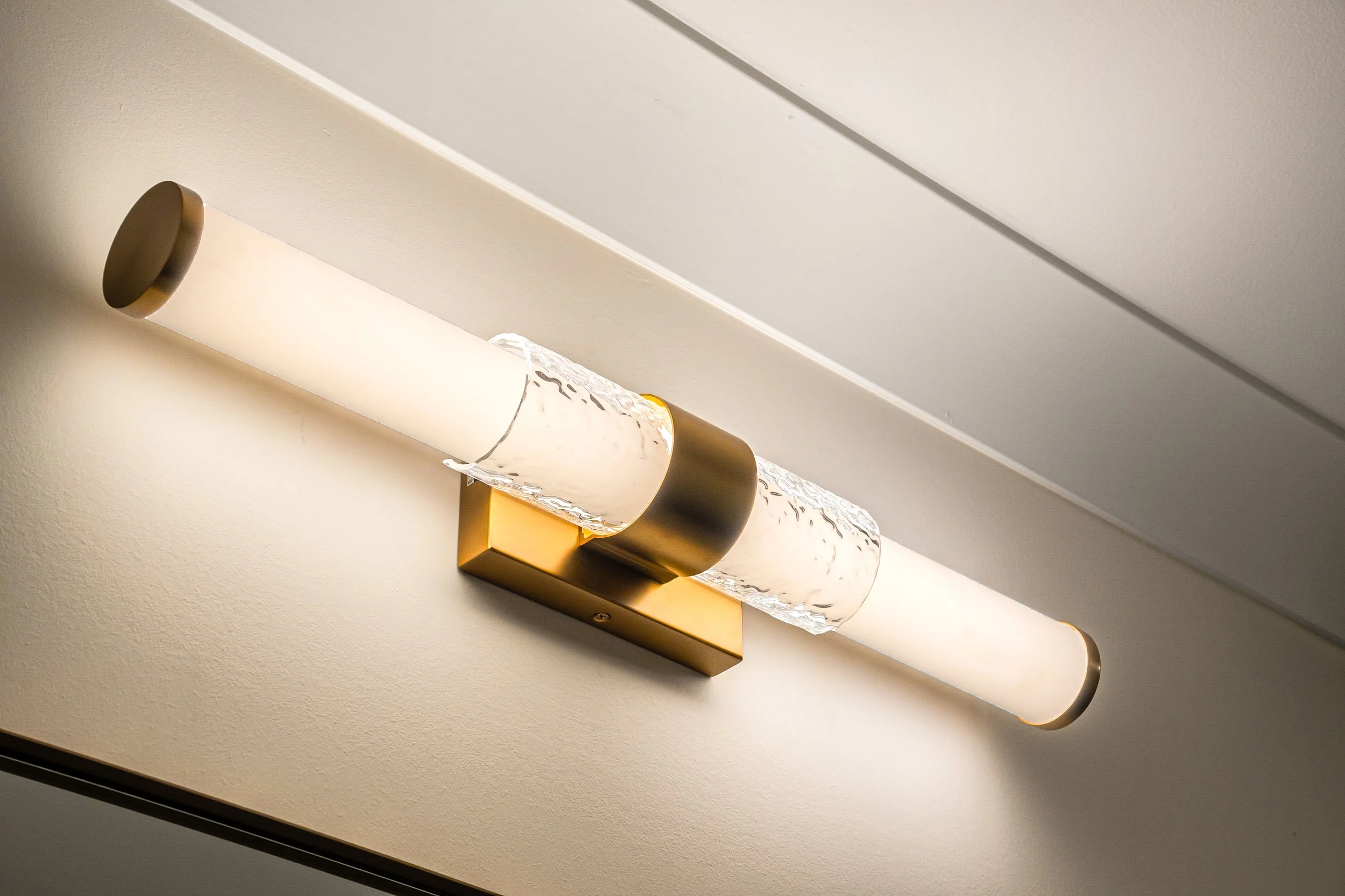 A modern wall-mounted light fixture with a curved glass shade and a brass base, mounted on a plain wall.