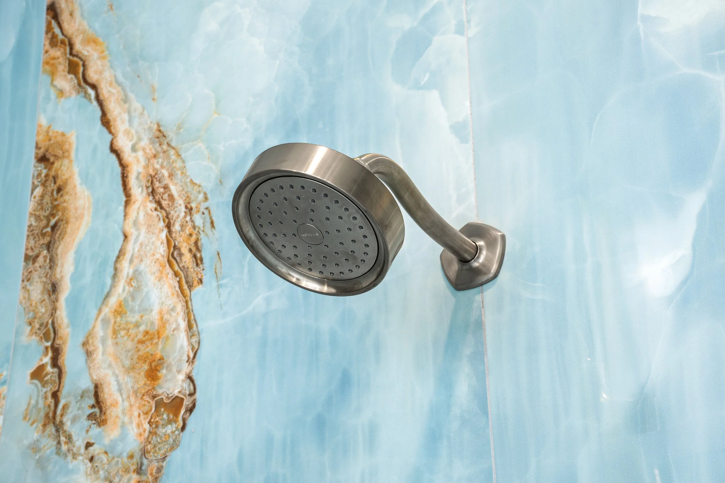 A silver showerhead attached to a wall with blue marble tiles.