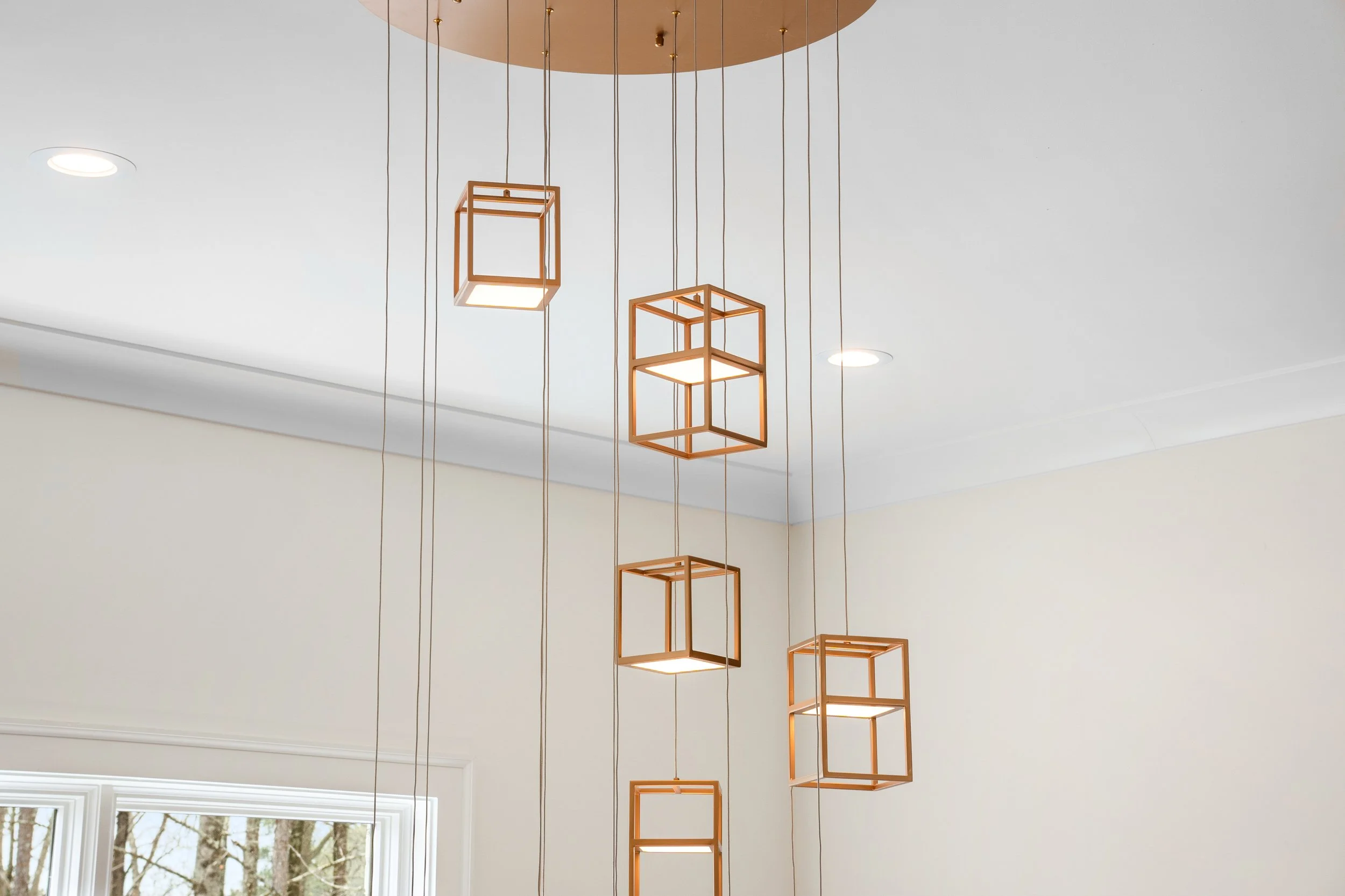 Modern geometric pendant light fixtures hanging from a round ceiling mount in a well-lit room with large windows.