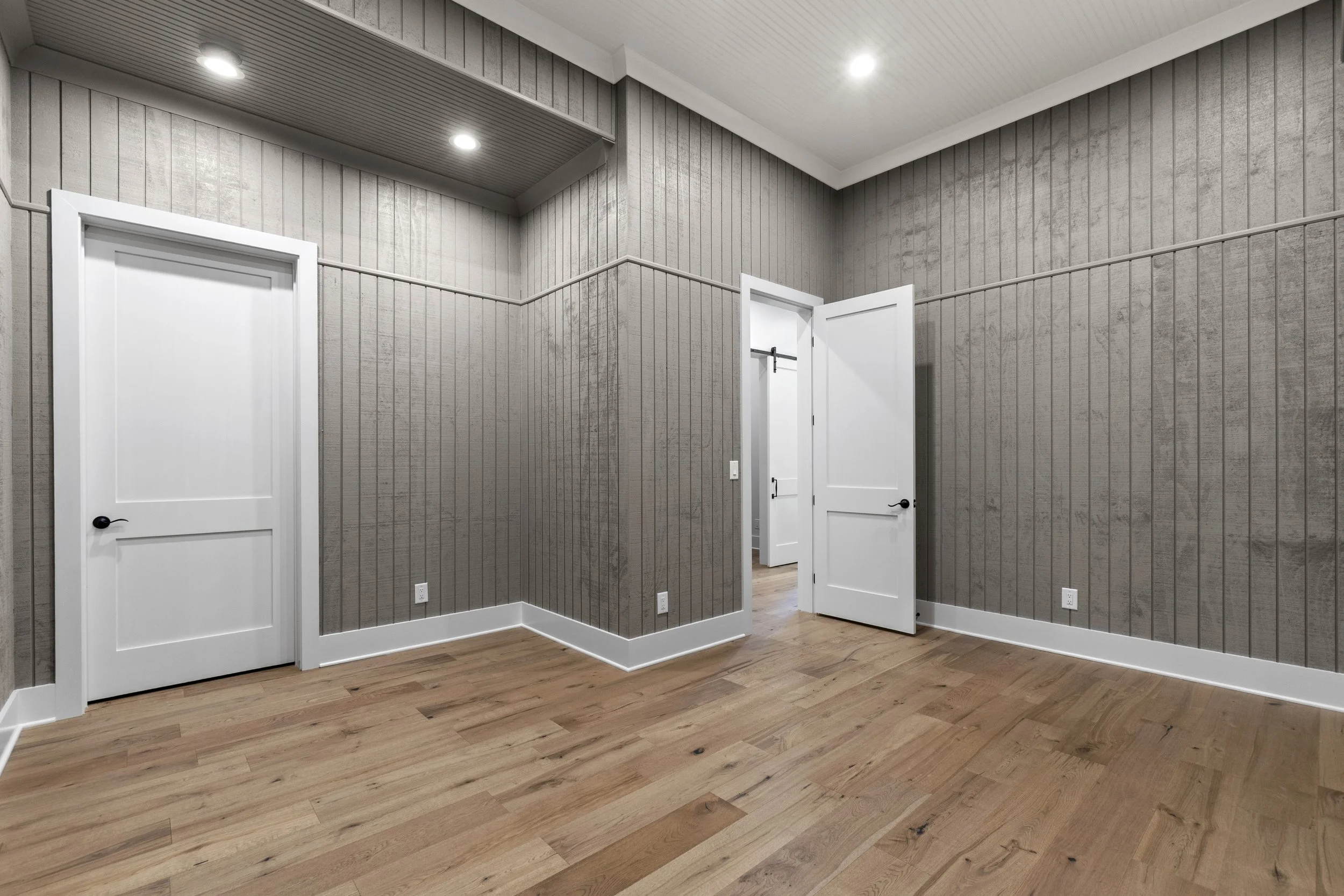 Interior of a room with gray textured walls, white doors, and wooden flooring, illuminated by ceiling lights.