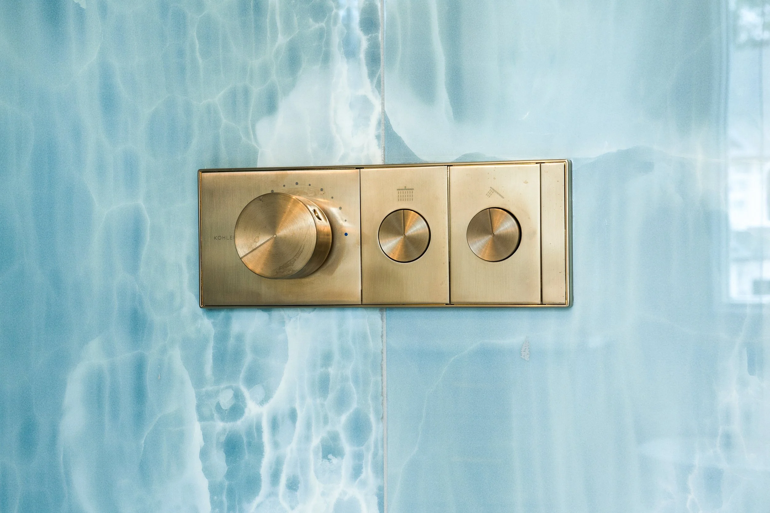 Close-up view of a stainless steel dual flush toilet button panel on a wall with light blue marble pattern.