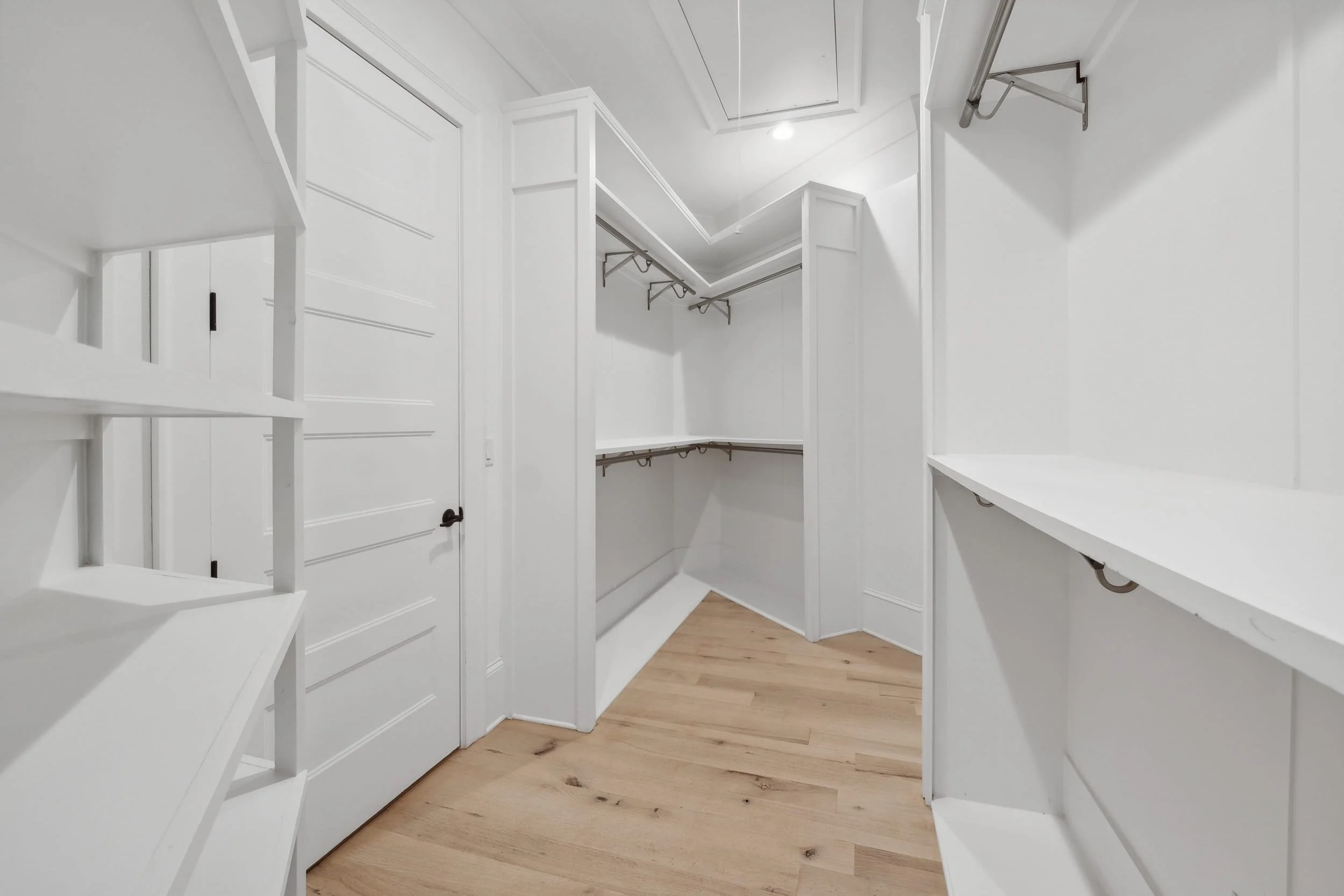 Empty walk-in closet with white shelves and wooden floor.