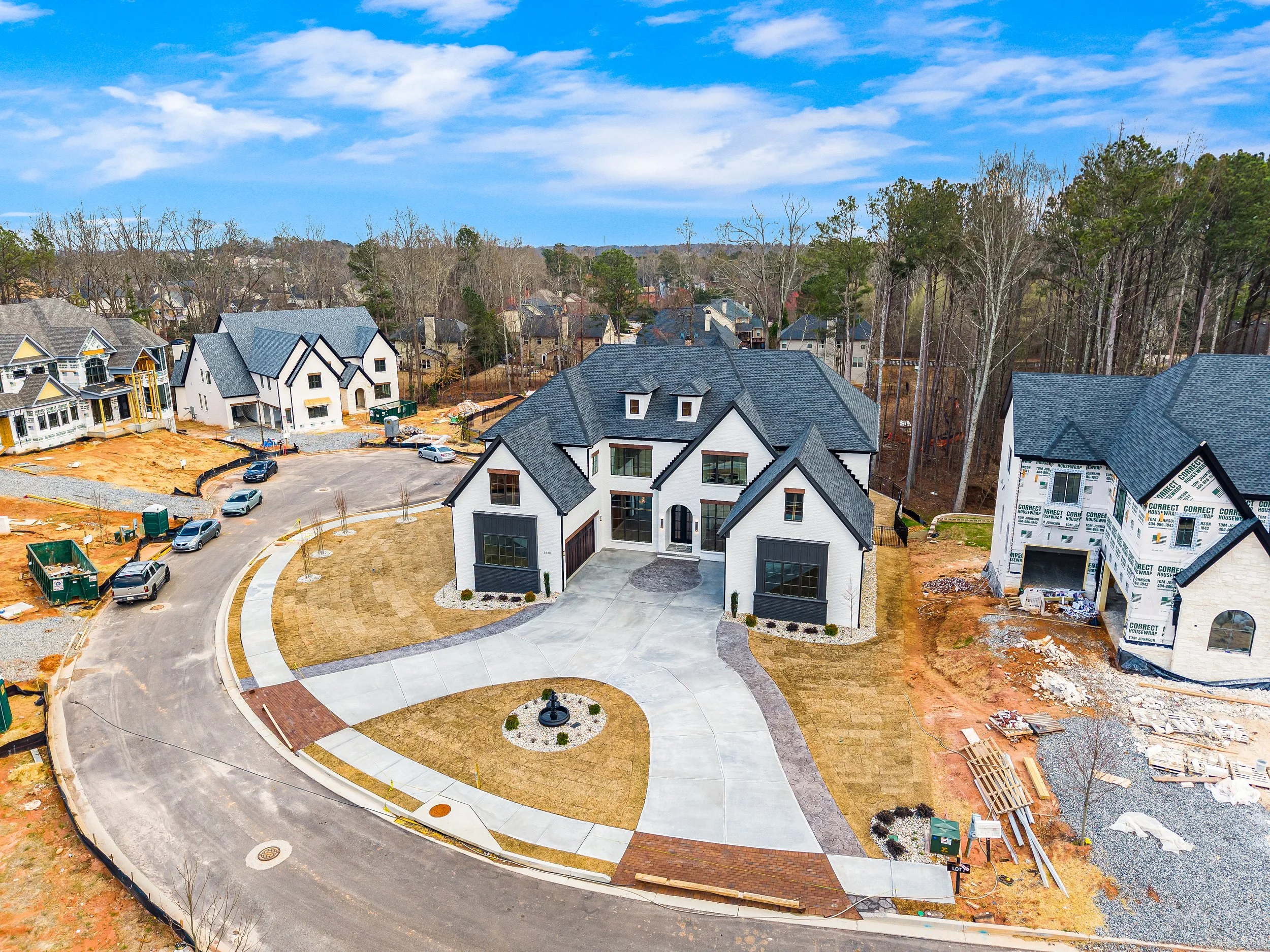 A neighborhood with new houses under construction, a roundabout with a fountain in the center, and a partly cloudy sky overhead.