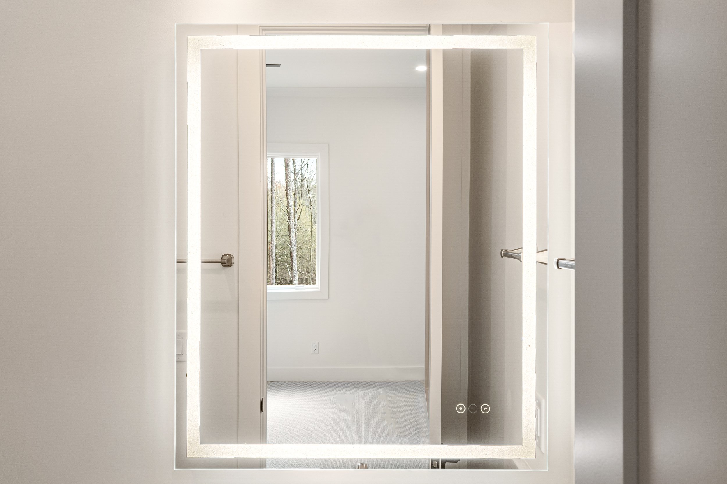 View of multiple elevator doors reflecting in a large mirror with a window showing trees outside in the background.