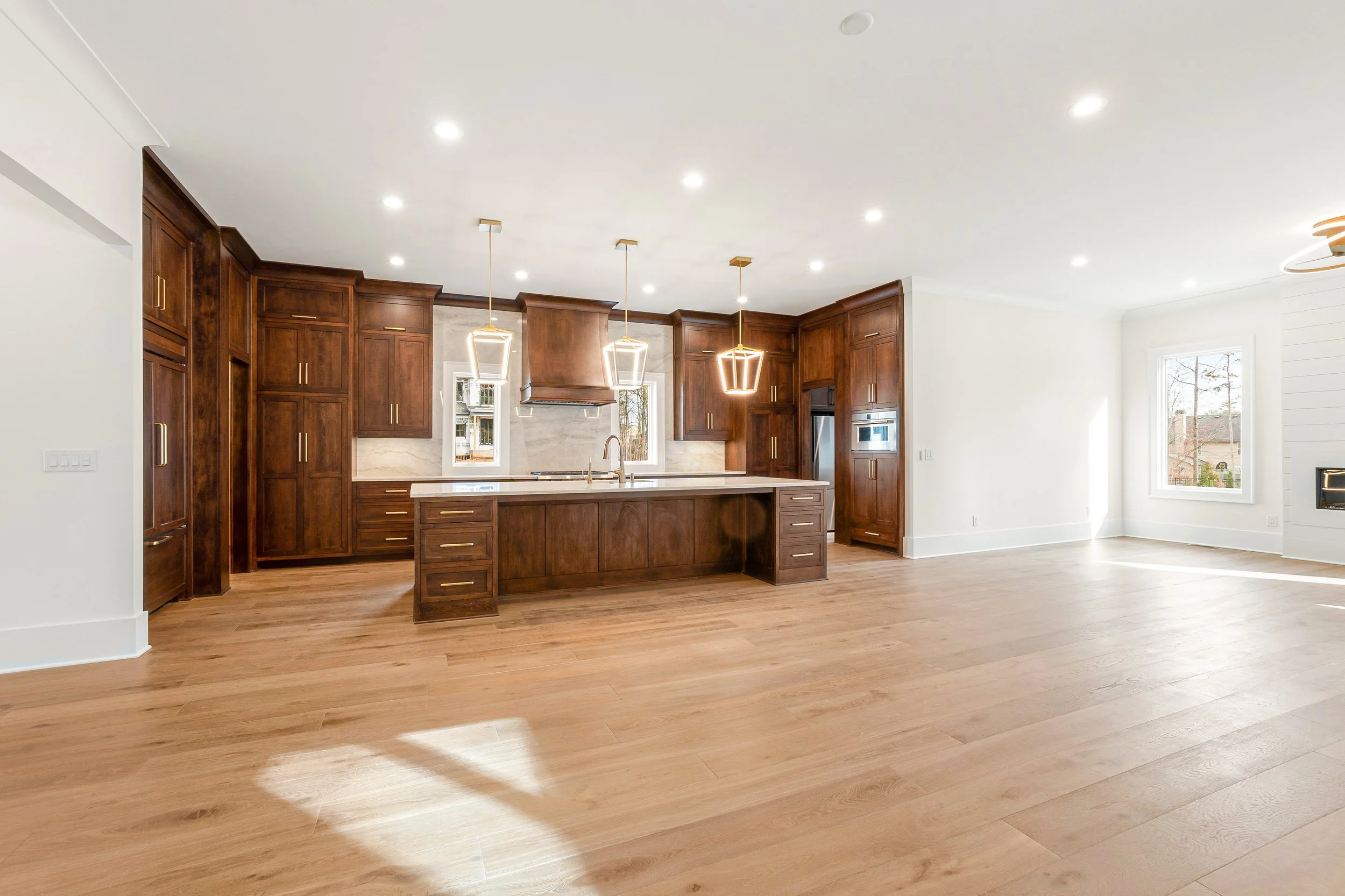Modern kitchen with dark wooden cabinets, a kitchen island, hardwood floors, large windows, and bright ceiling lights.