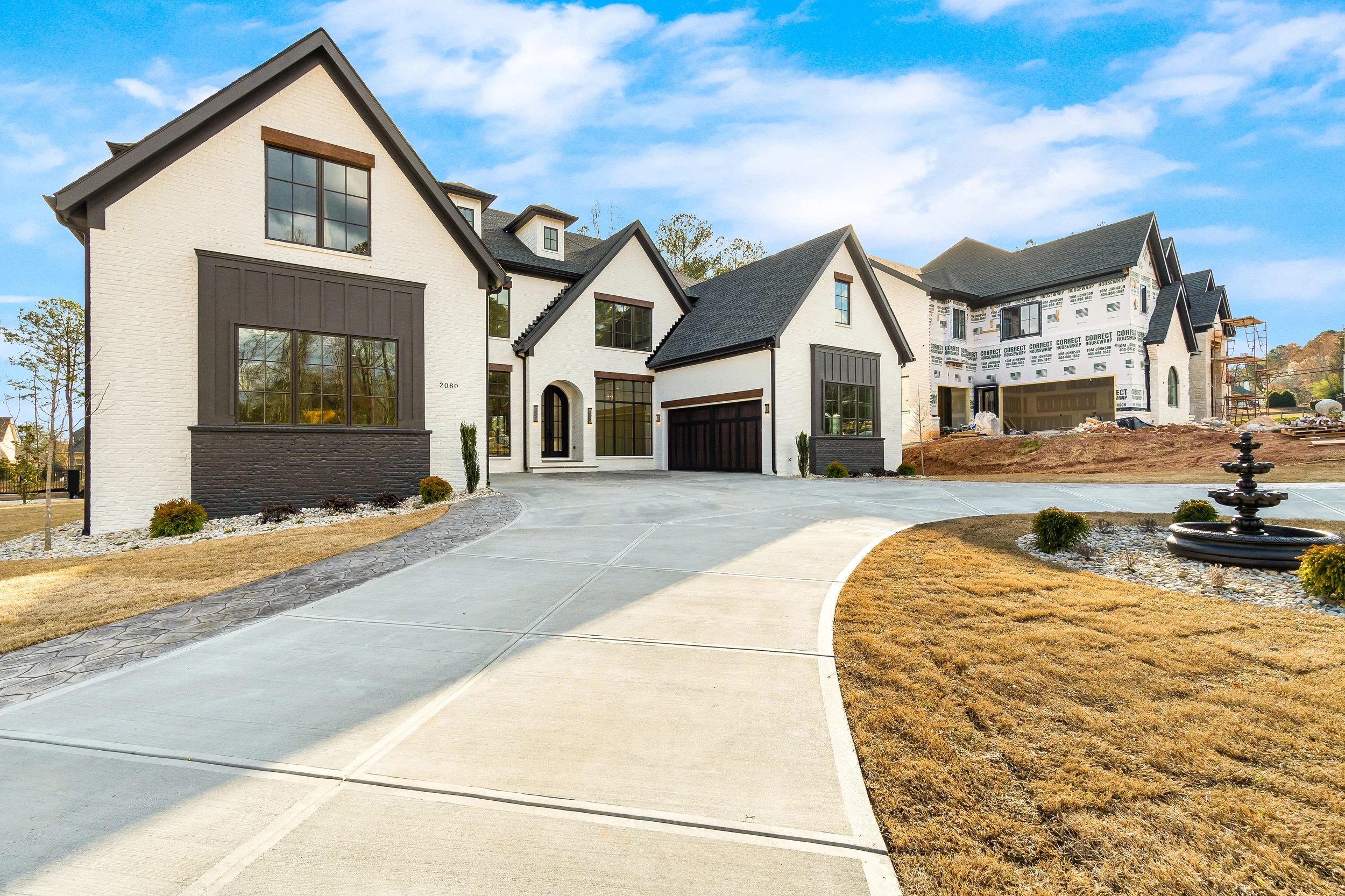 Newly constructed modern house with white brick exterior, black window frames, and a dark gray roof, under a clear blue sky.