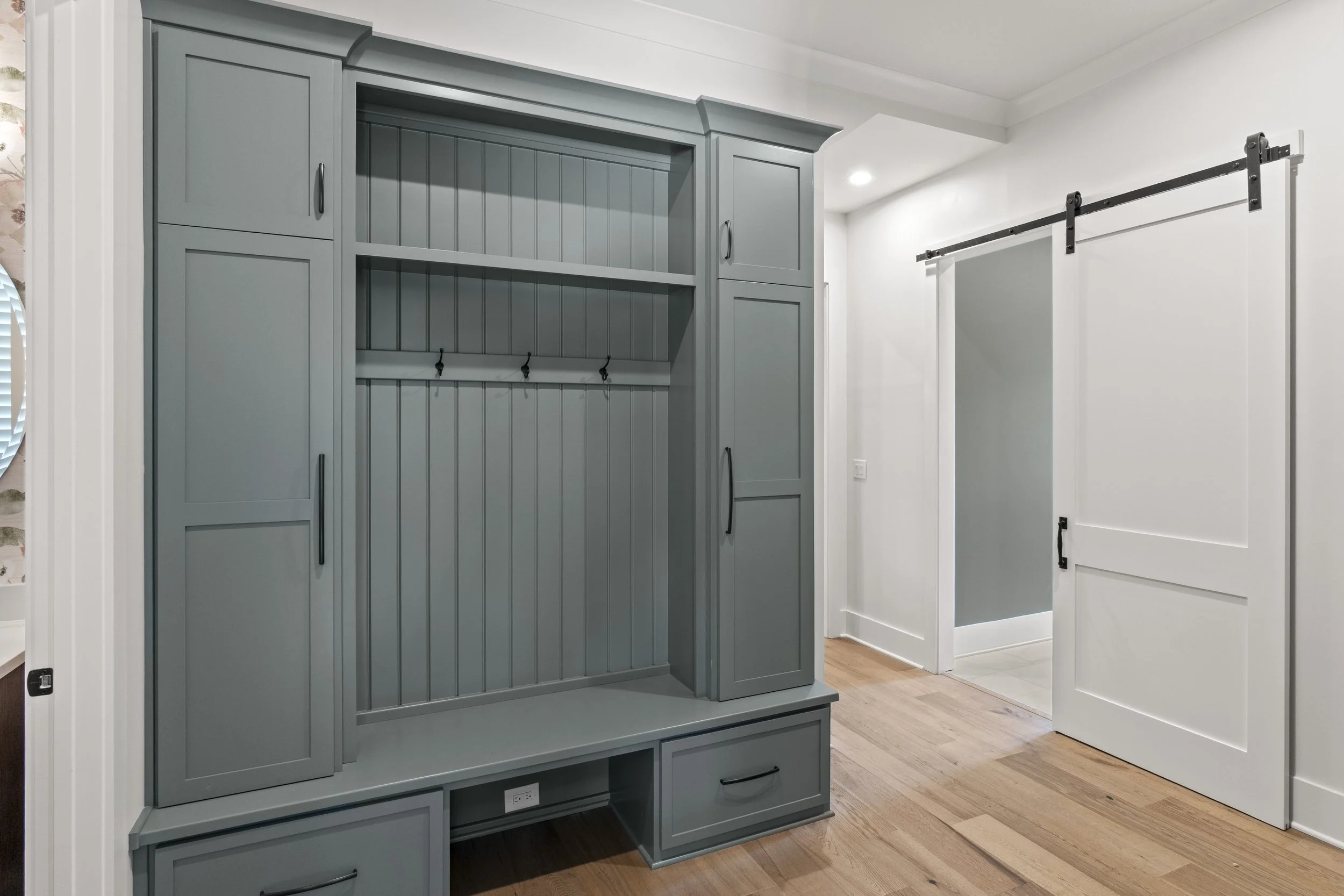 Gray built-in cabinet with open shelving and closed storage doors, located next to a white sliding barn door in a room with hardwood flooring.