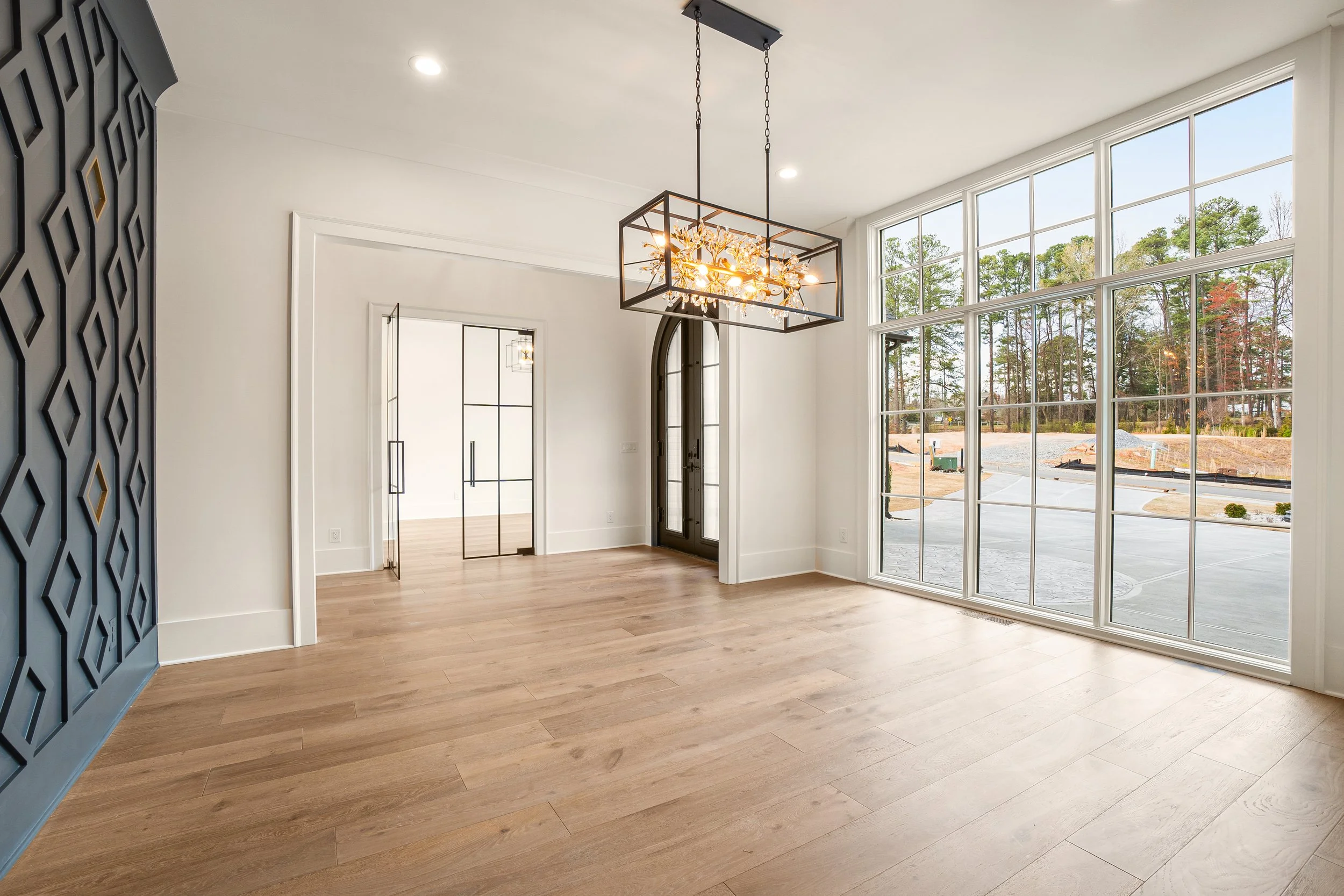 Bright, airy interior with large picture windows, modern chandelier, wood flooring, and white walls.