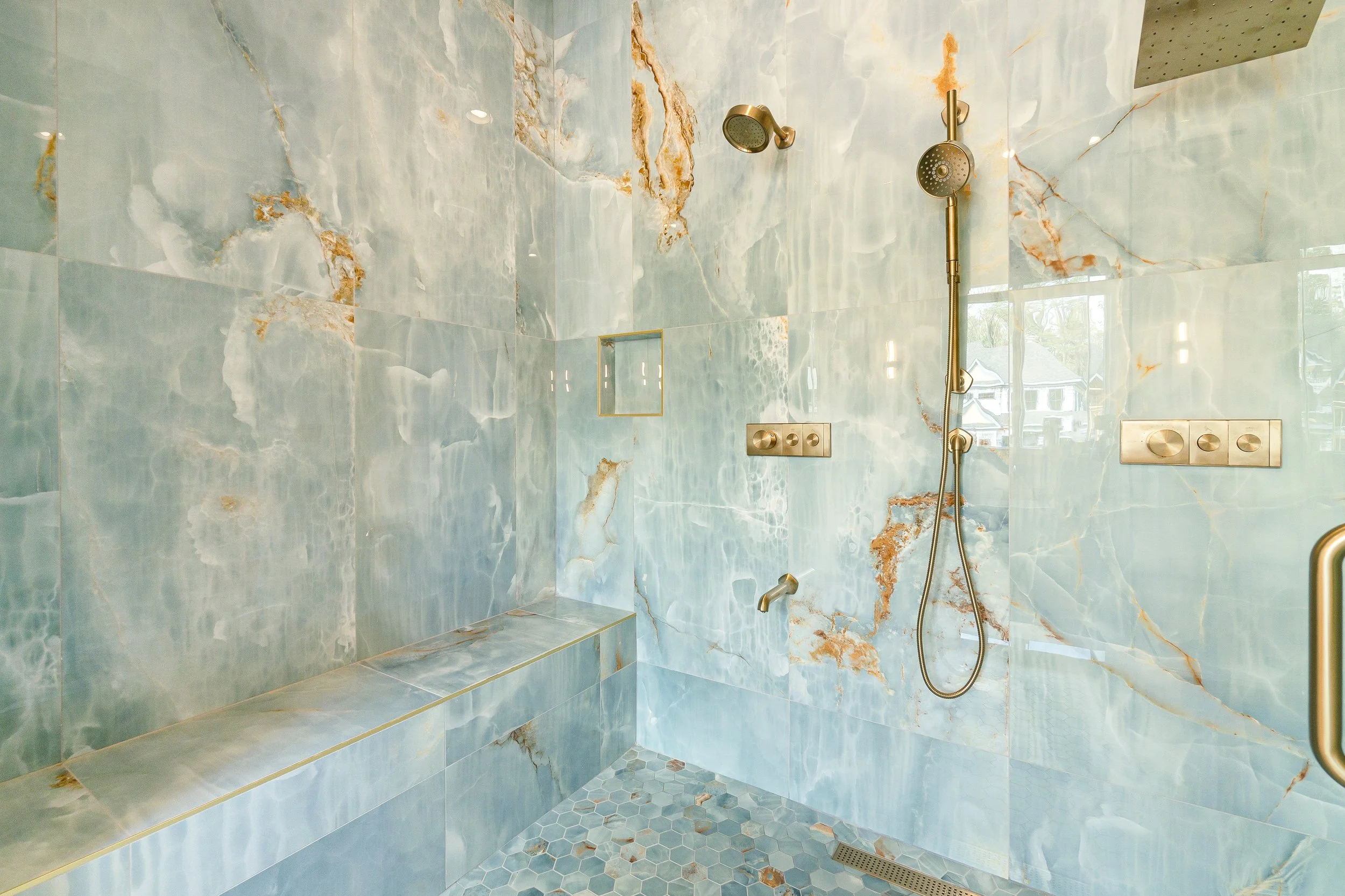 A walk-in shower with blue and orange marble tiles, built-in bench, dual showerheads, and a grab bar.