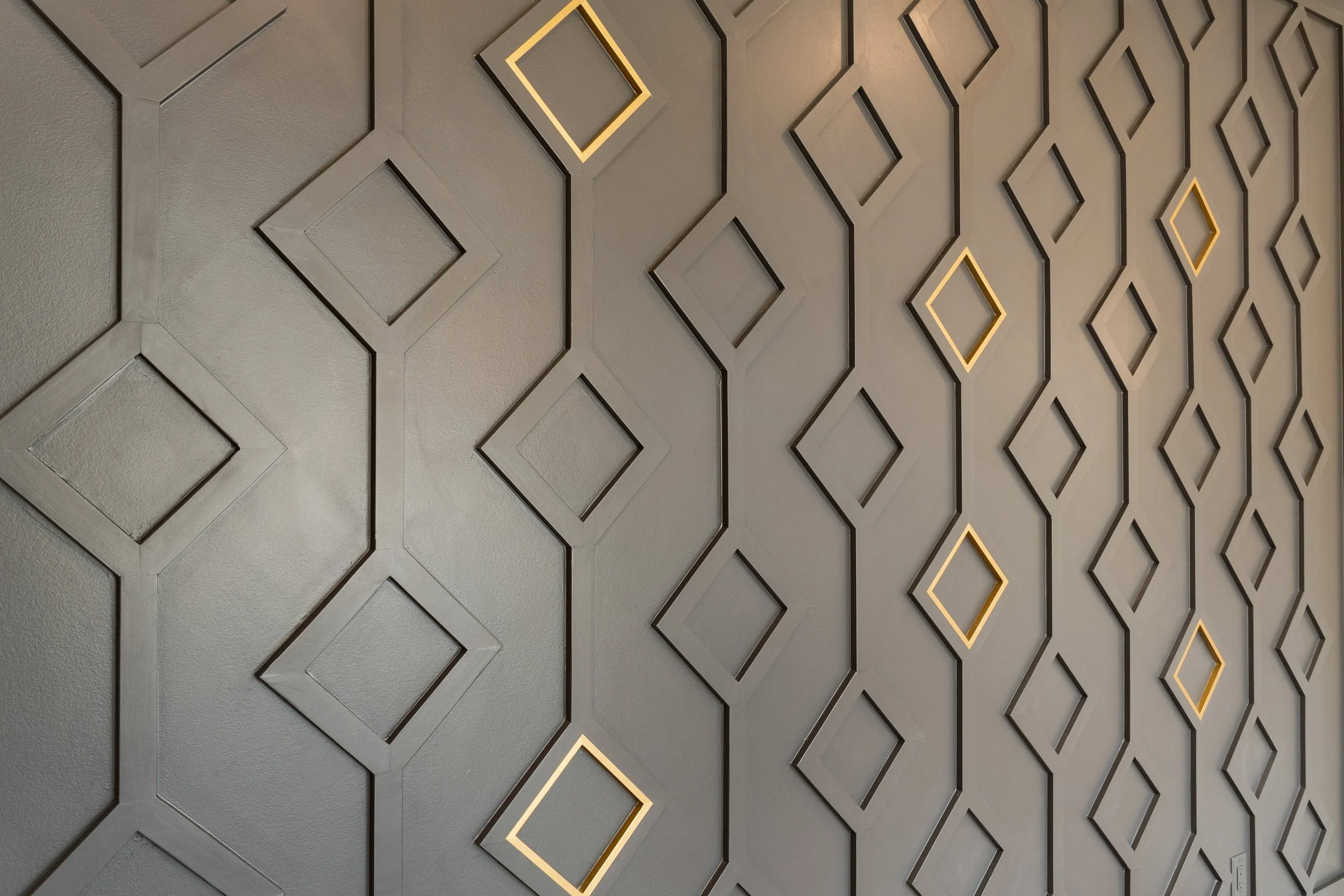 A decorative wall with geometric diamond-shaped patterns outlined with LED lighting, set against a textured wall.