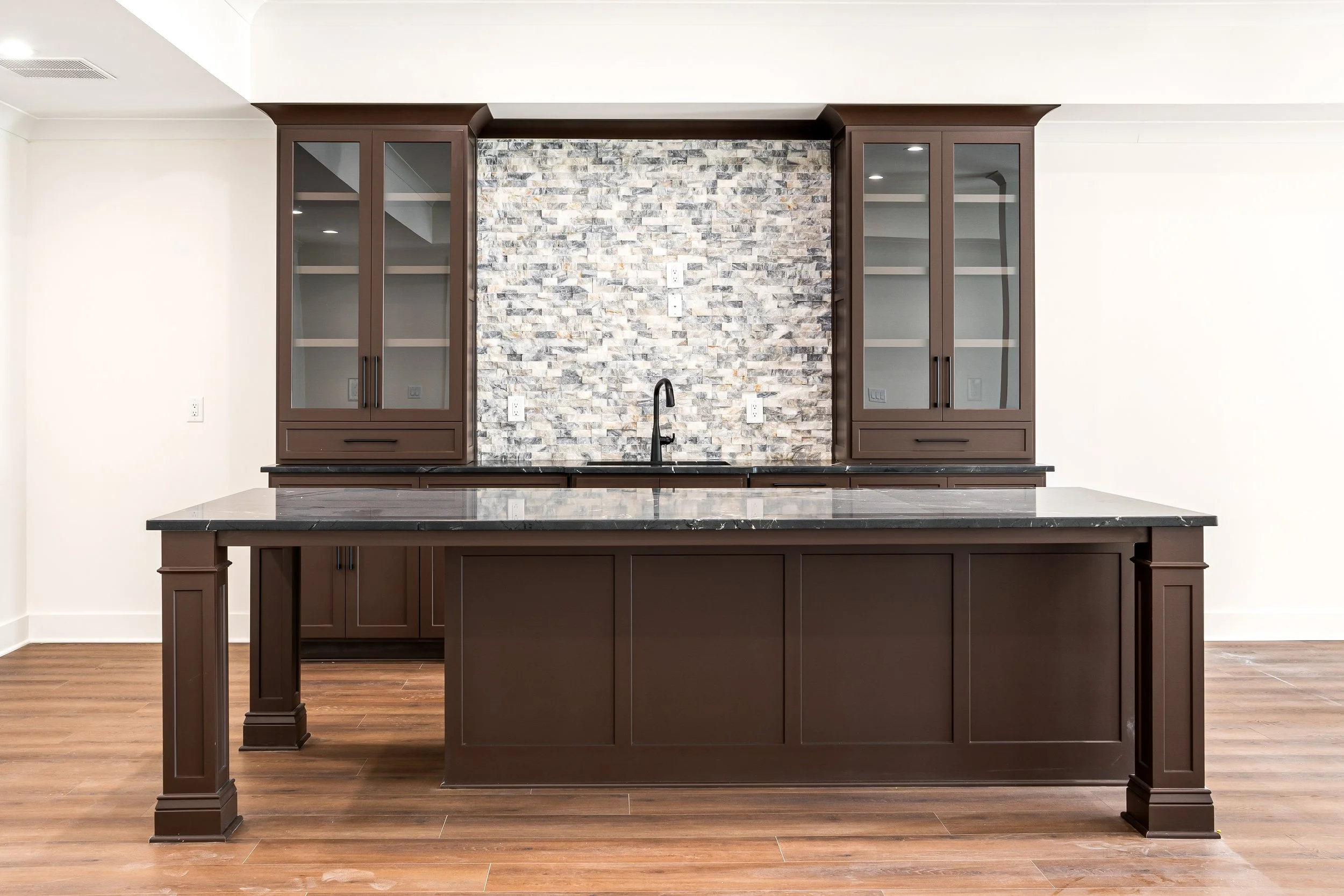 Kitchen with dark wood cabinets, a black marble island, a brick backsplash, and a black sink faucet.