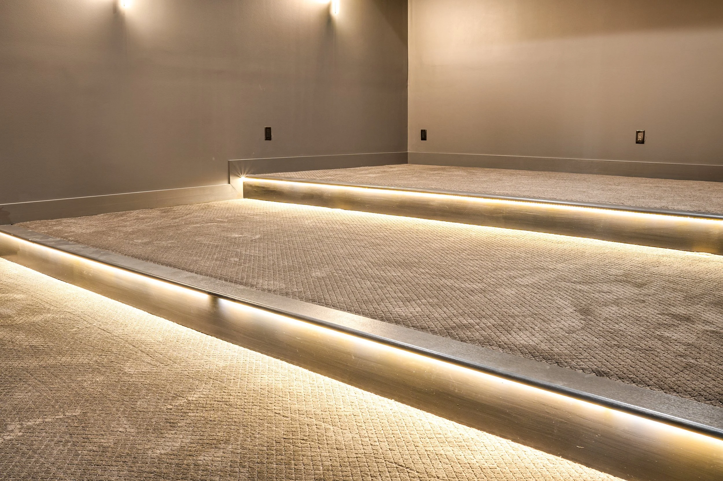 Empty room with gray walls, beige carpet, and a slightly elevated platform with LED lighting underneath.