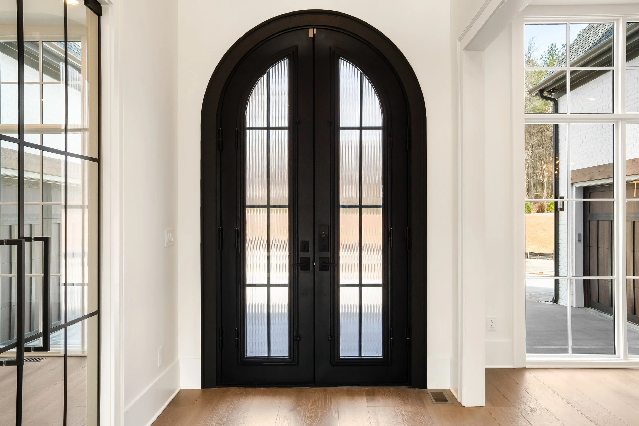 Black arched front door with sidelight windows on either side in a bright, modern entryway with white walls and hardwood flooring.