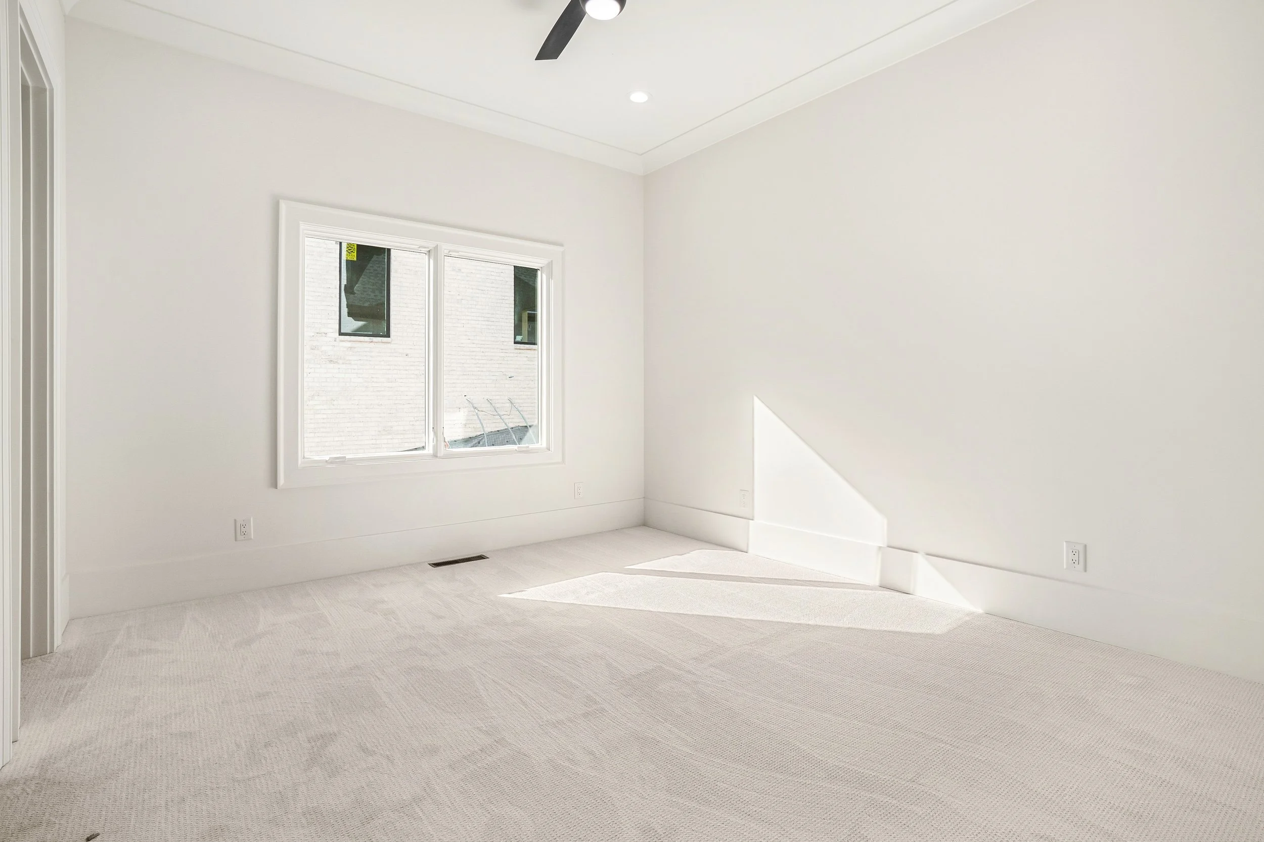Empty room with white walls, beige carpet, a window, ceiling fan, and a small window near the ceiling.
