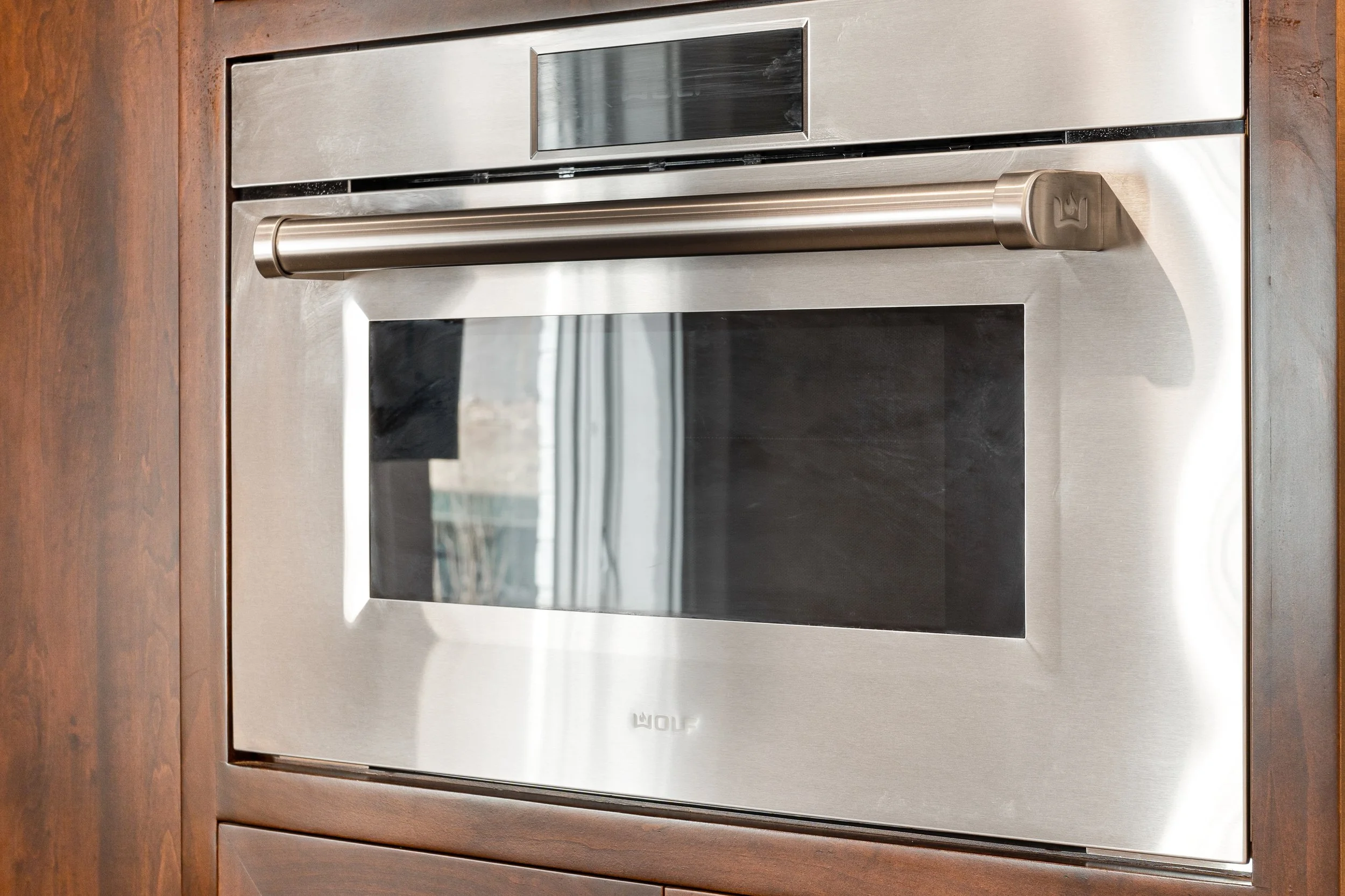 Stainless steel wolf oven built into a wooden cabinet.