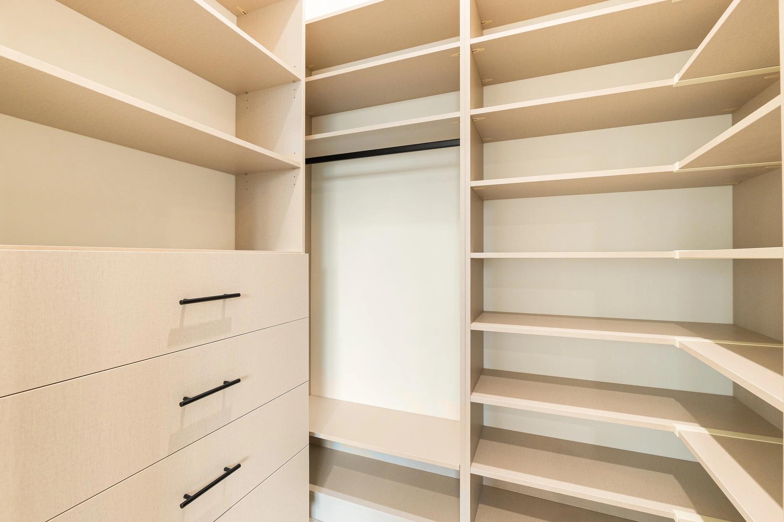 Empty white closet with shelves and drawers, viewed from an angle.