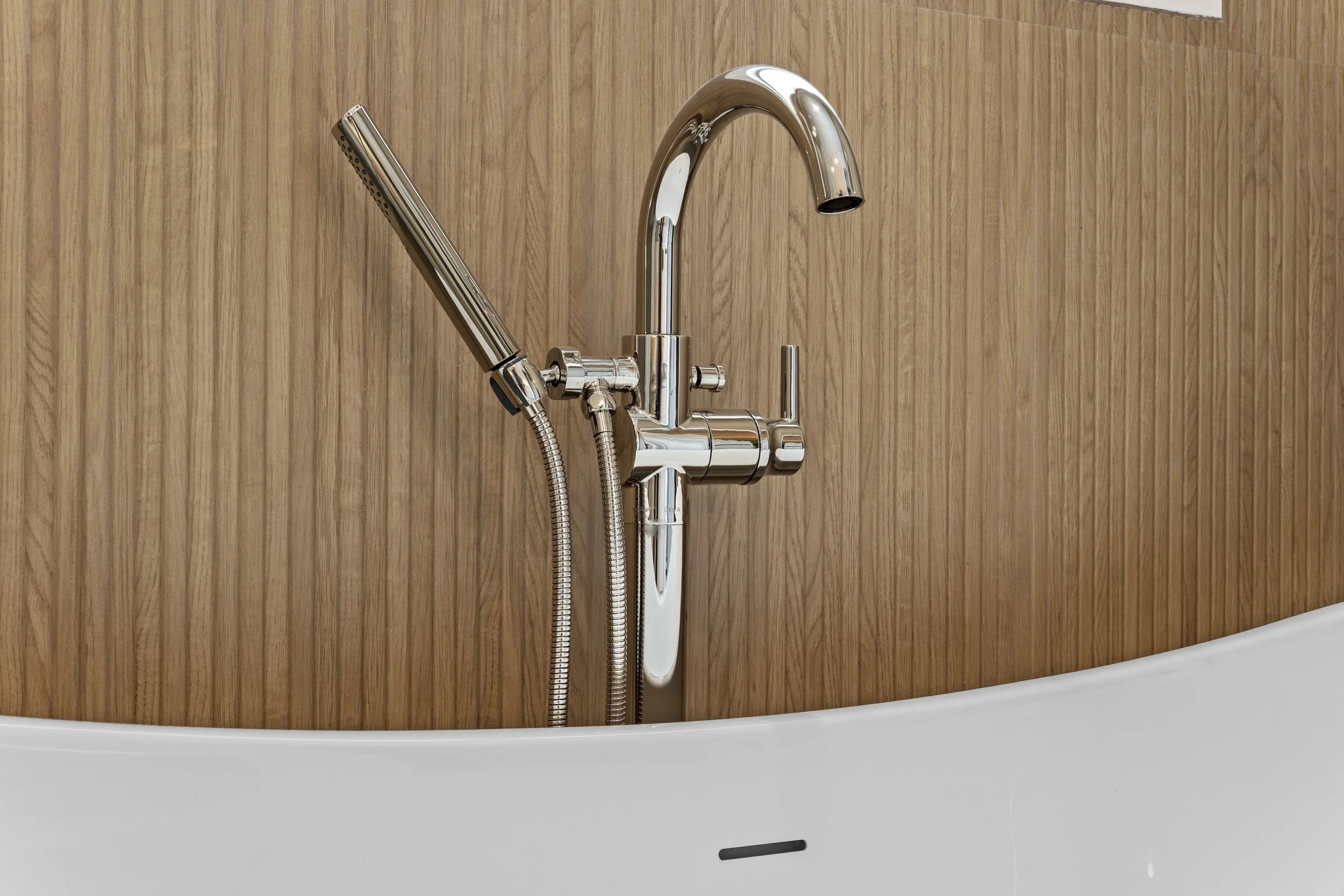 A modern kitchen faucet with a shiny chrome finish mounted on a wooden backsplash.