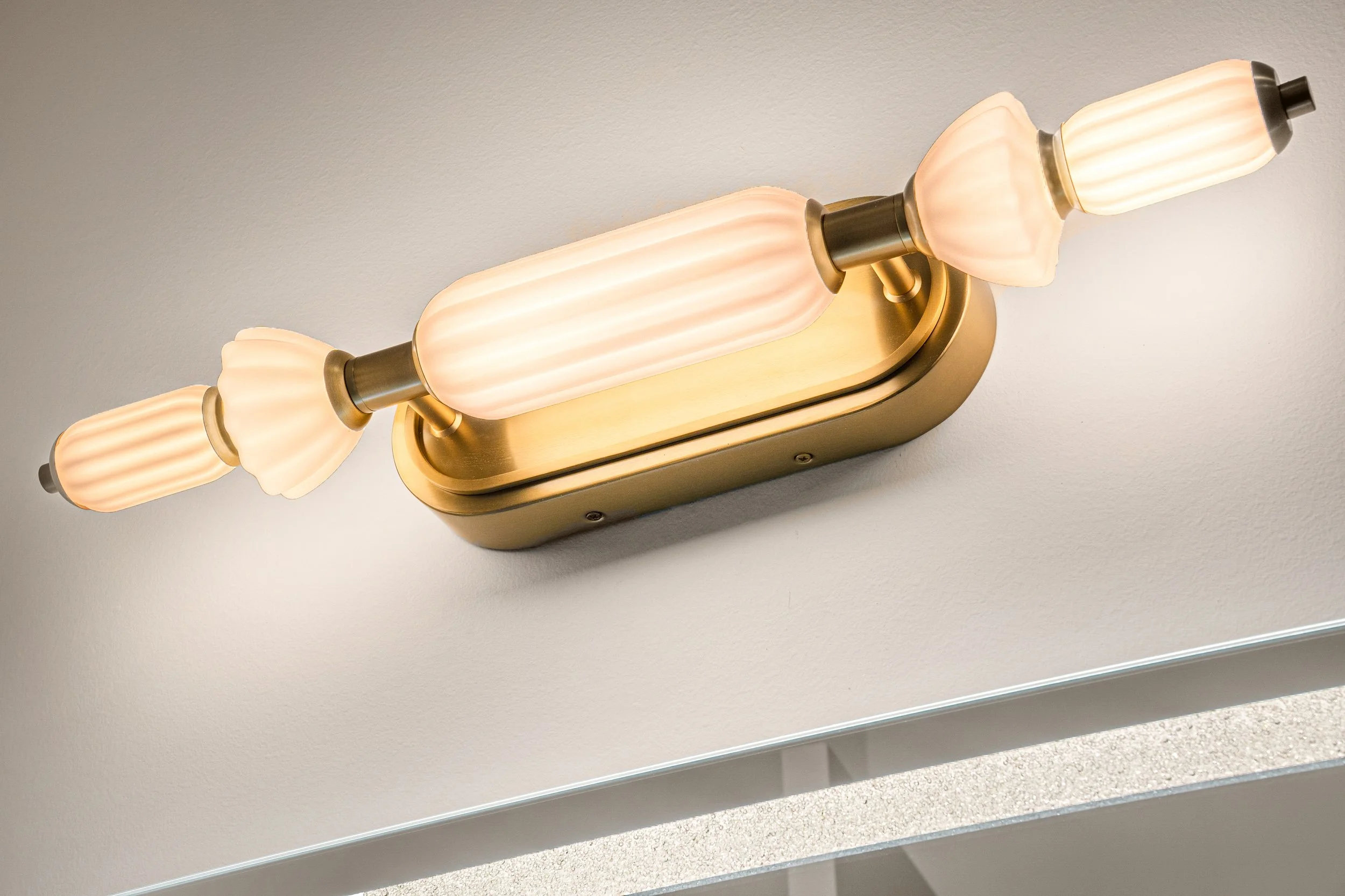 Close-up of a modern wall-mounted light fixture with three frosted glass shades and brass accents, installed on a white wall.