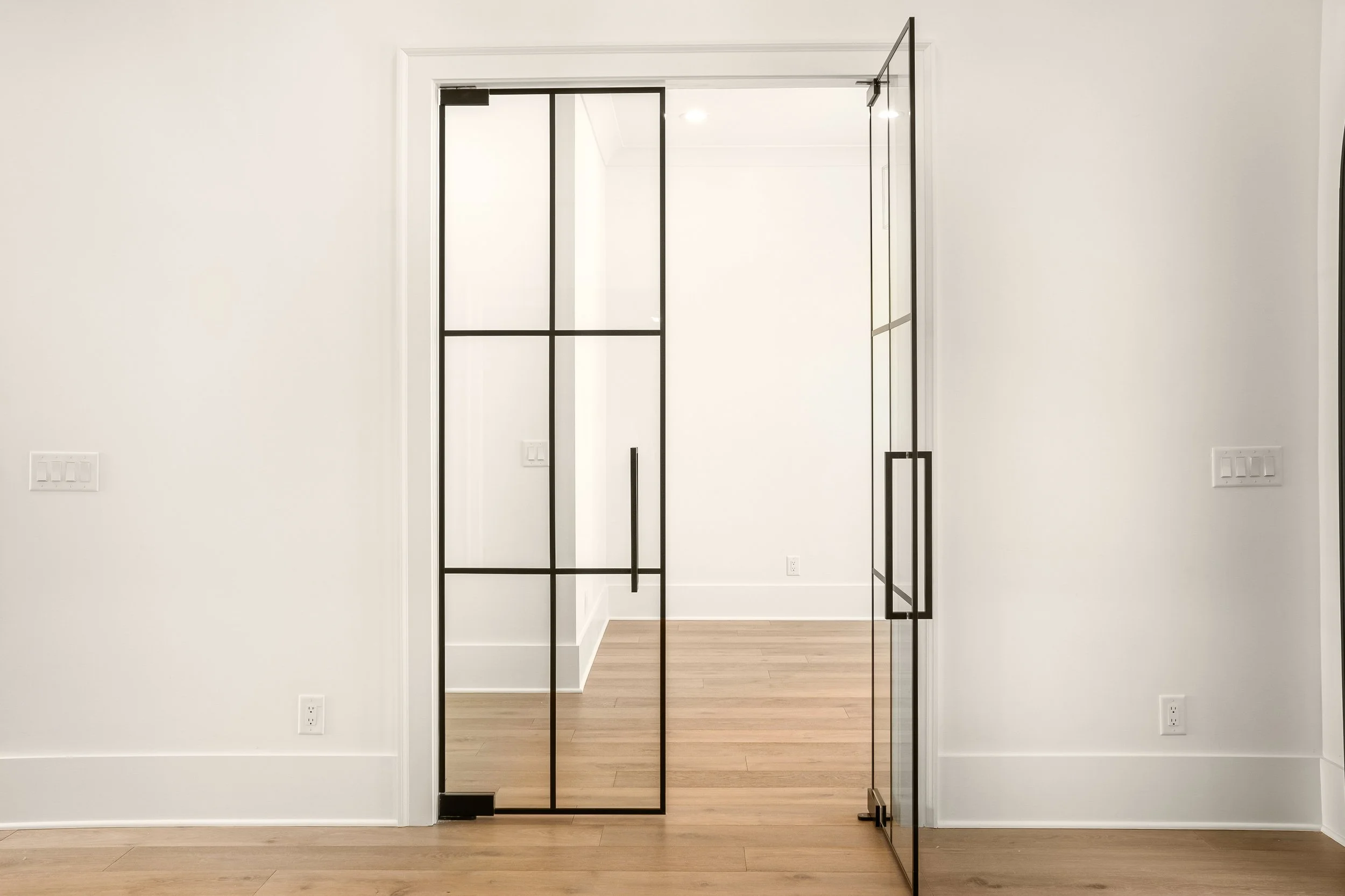 Modern interior with glass sliding door, white walls, wood flooring, and electrical outlets.