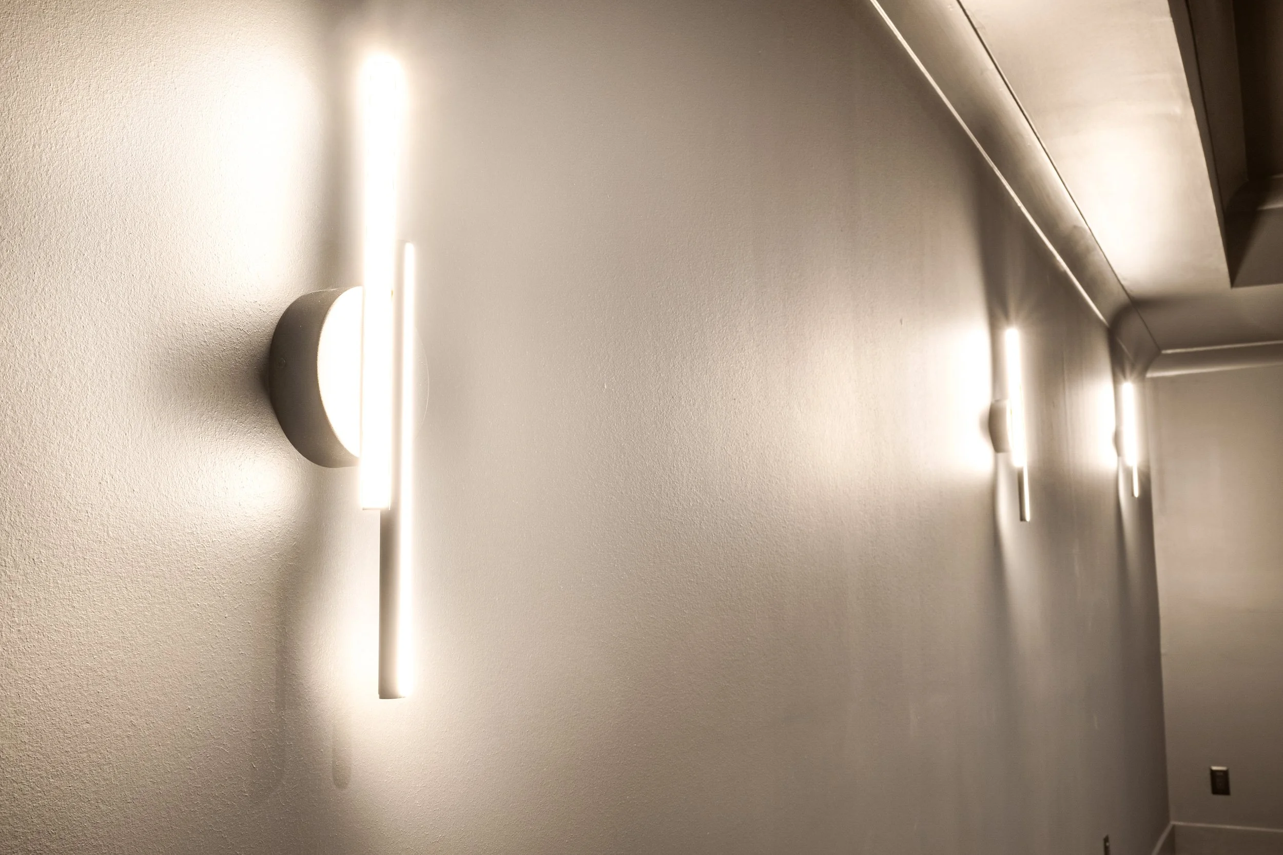 Modern wall-mounted lights on a textured wall in a hallway or corridor.