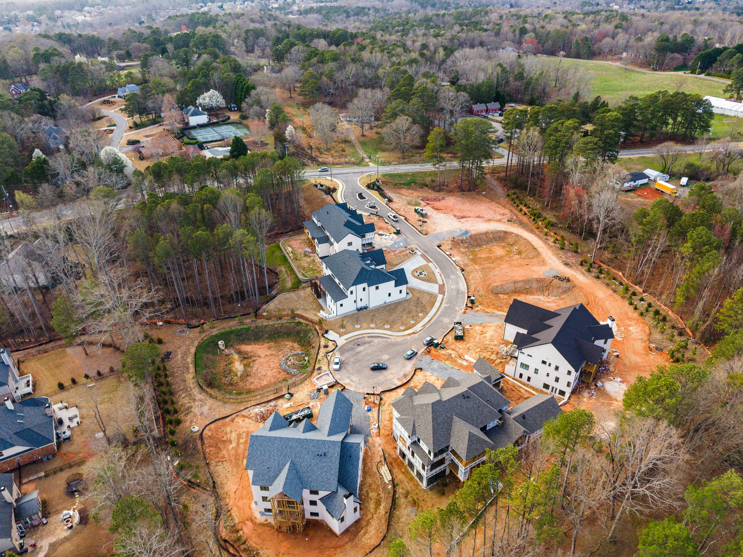 Aerial view of a residential neighborhood with houses, trees, and ongoing construction site with cleared earth and building framework