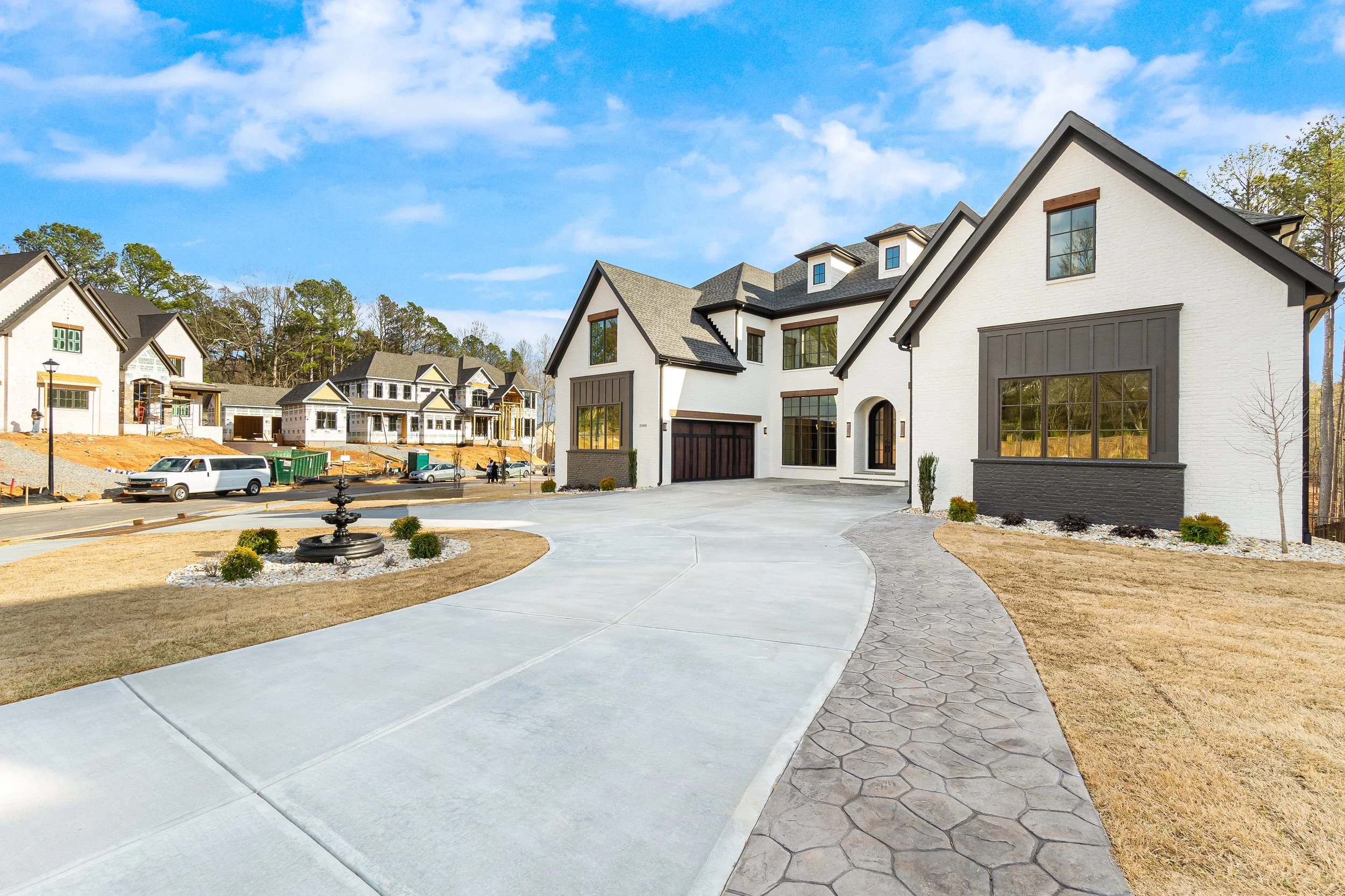 Suburban neighborhood with new modern-style houses under construction, parked cars, and a partly cloudy sky.