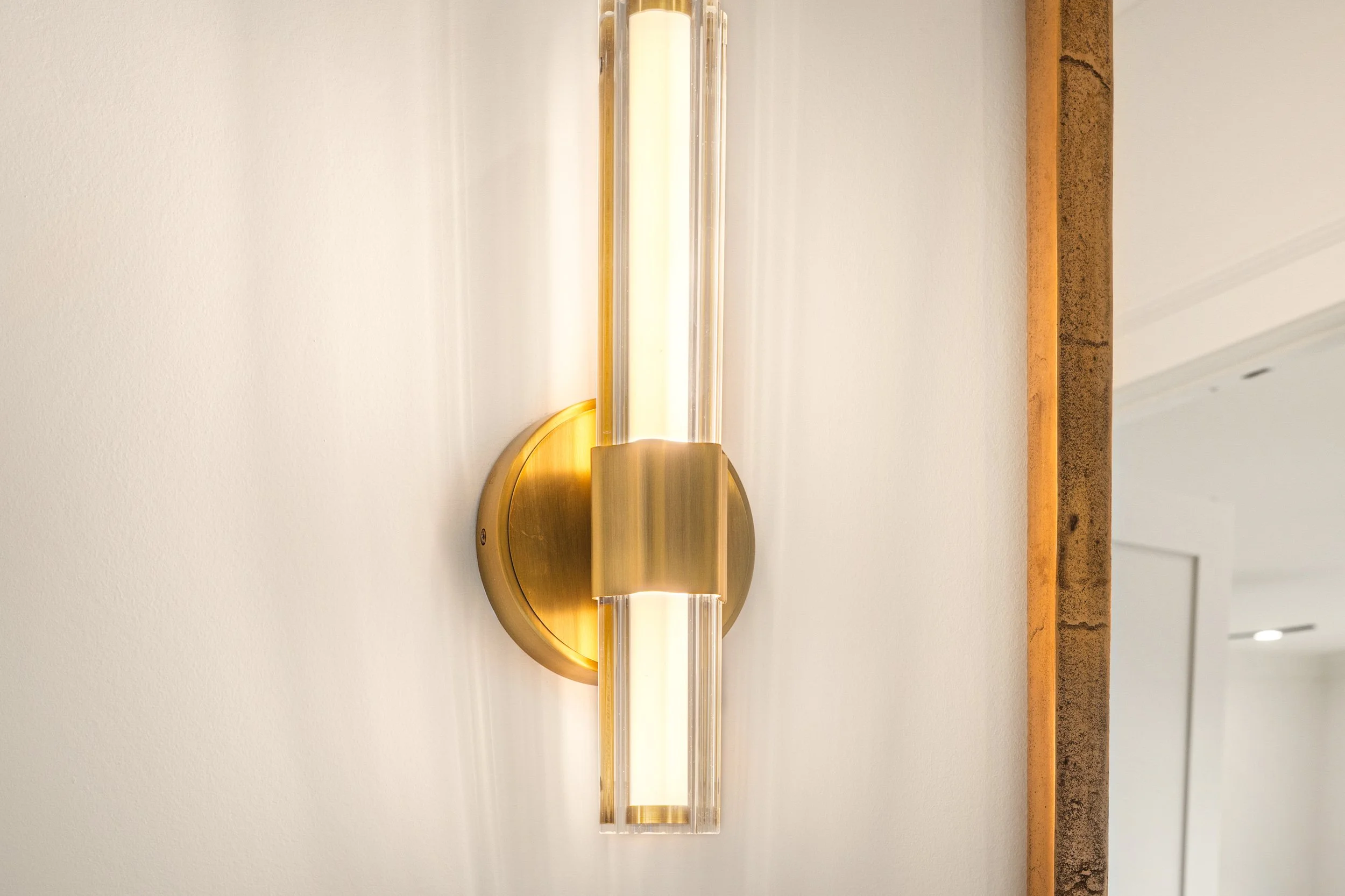 Modern wall-mounted light fixture with a cylindrical frosted glass shade and brass-colored metal accents, mounted on a white wall.