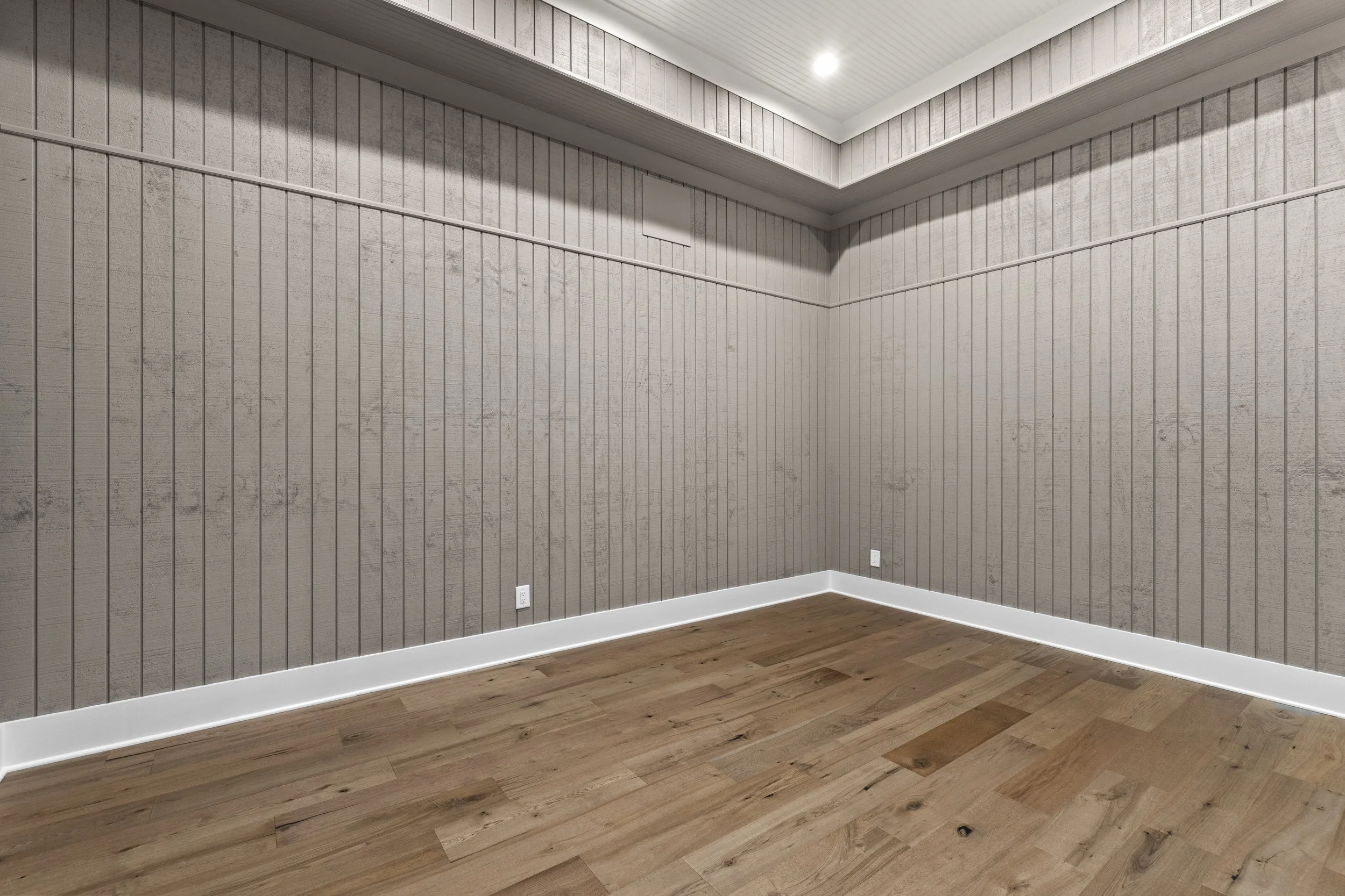 Empty room with wood flooring, beige wood-paneled walls, white baseboard, and ceiling with recessed light.