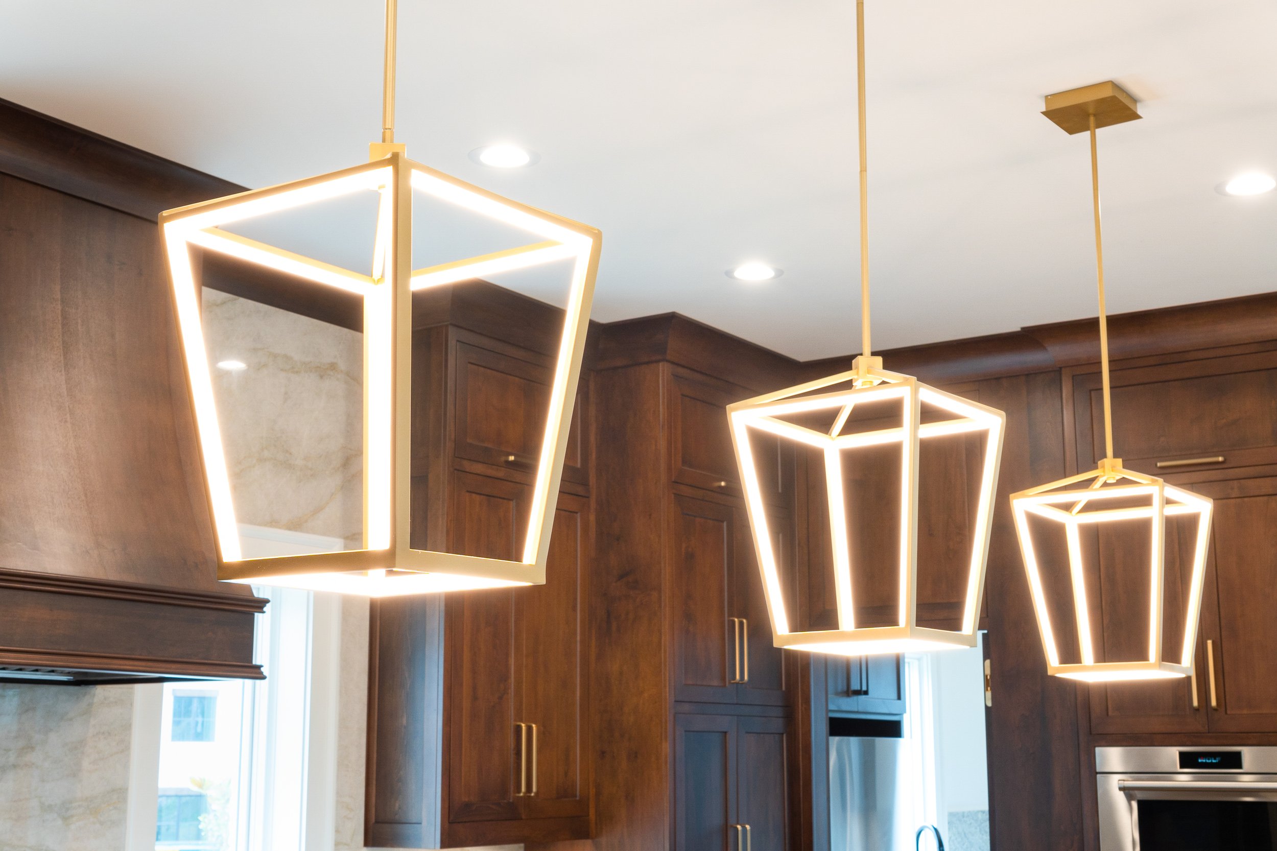 Modern kitchen with wooden cabinets and geometric pendant lights hanging from the ceiling.