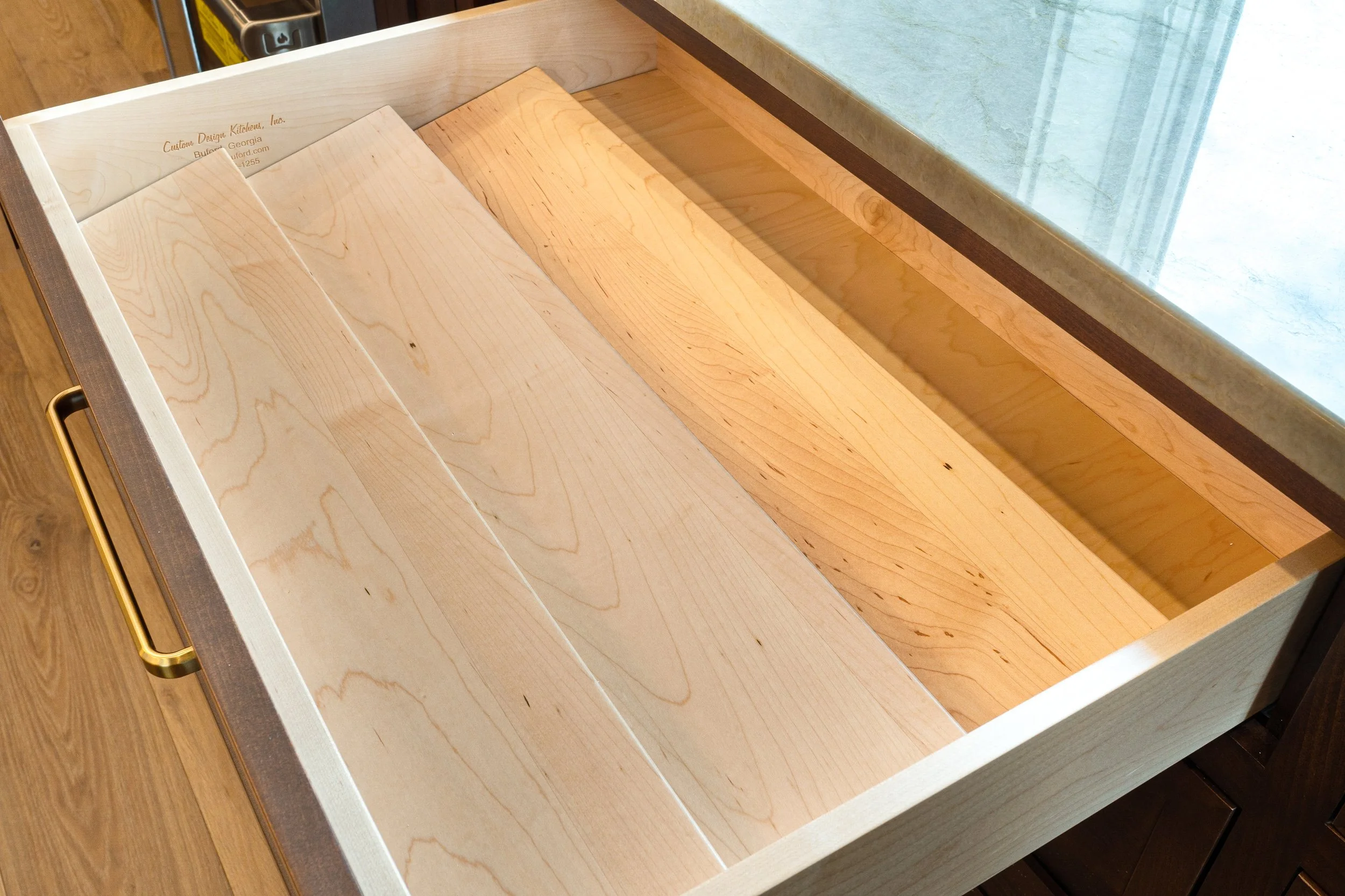 A wooden drawer with a light wood finish and a gold handle.