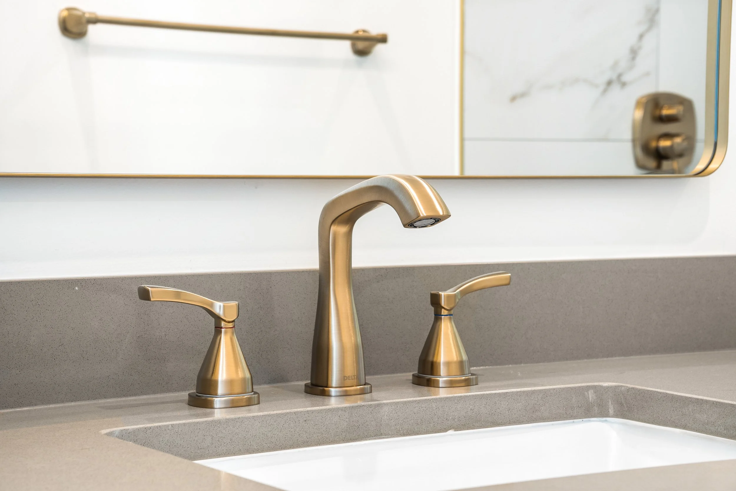 A bathroom sink with a gold faucet and separate handles, a mirror with a gold frame, and a towel rack on the wall.