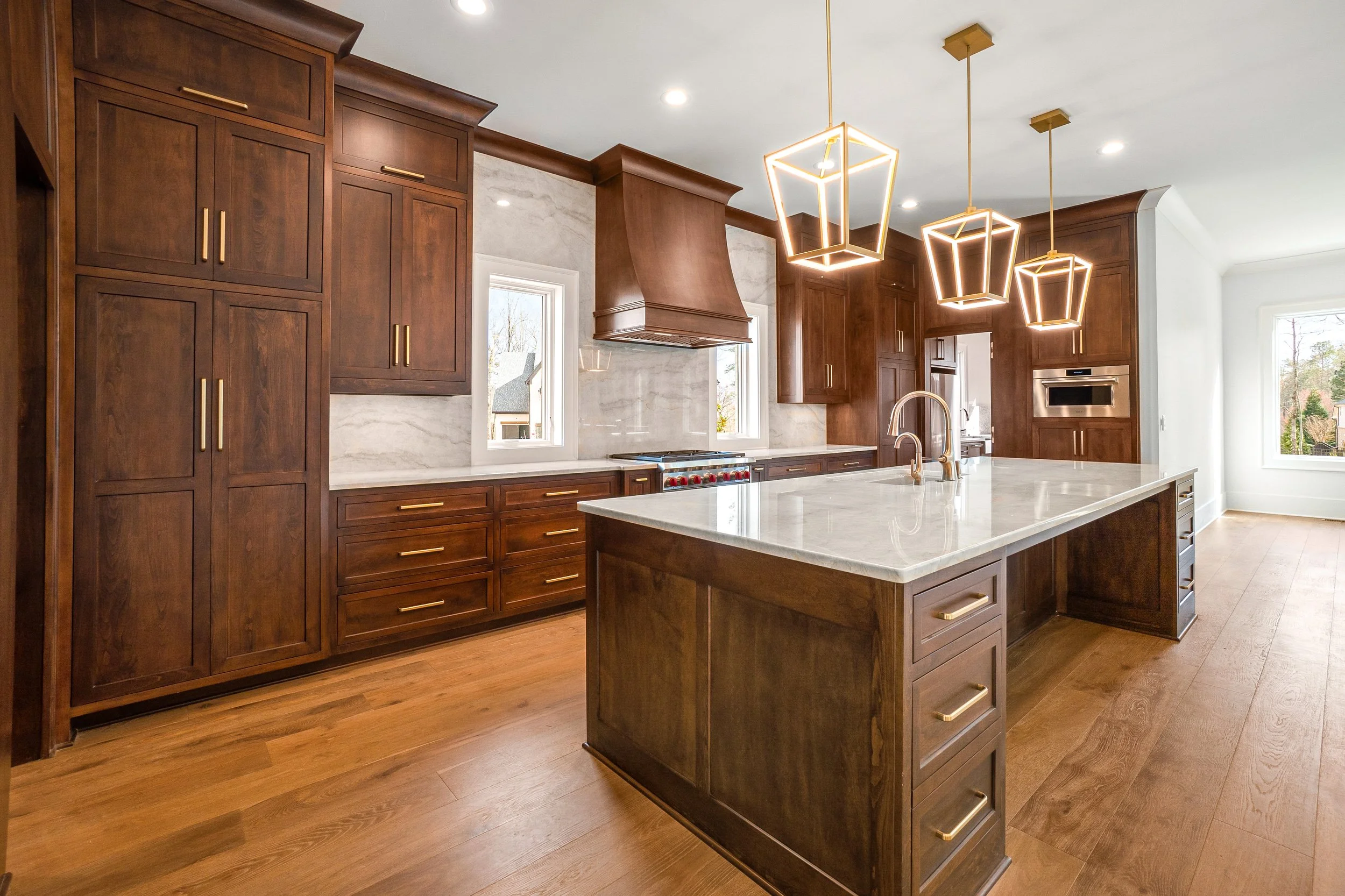 Modern kitchen with wooden cabinets, a large marble island, and pendant lights.