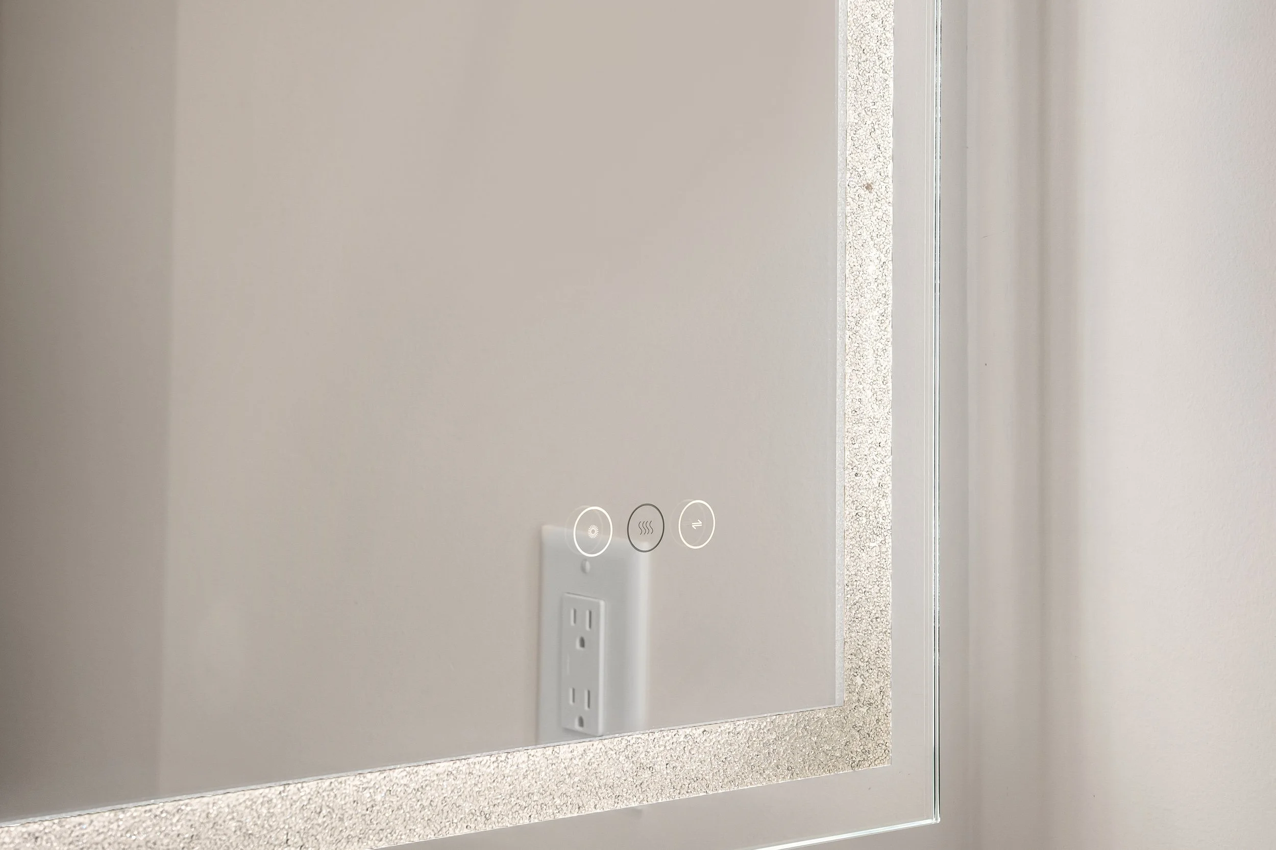 Close-up of a white wall with a built-in electrical outlet and control panel with three touch buttons, set in a kitchen or bathroom countertop with a textured, speckled surface.