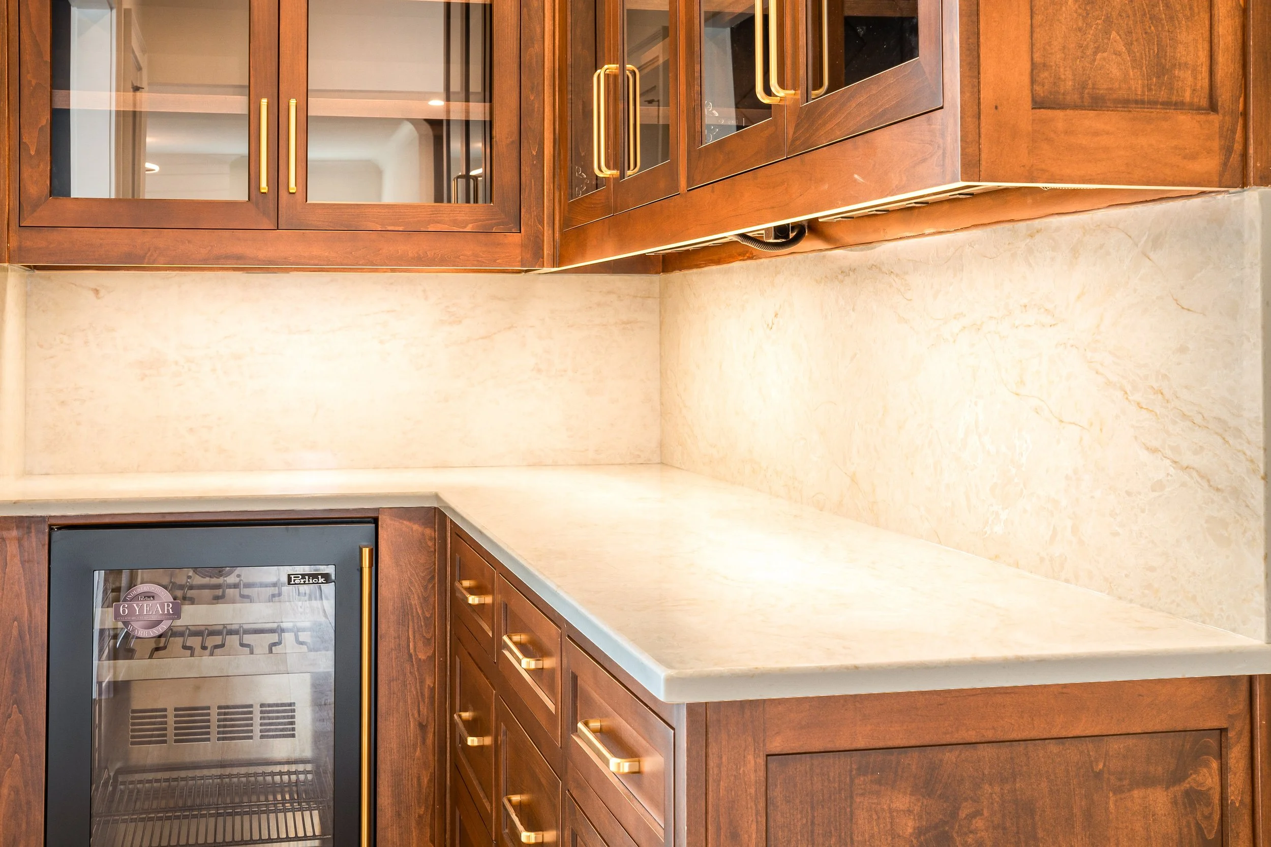 A kitchen with wooden cabinets, a beige marble countertop, and a small wine fridge built into the cabinetry.