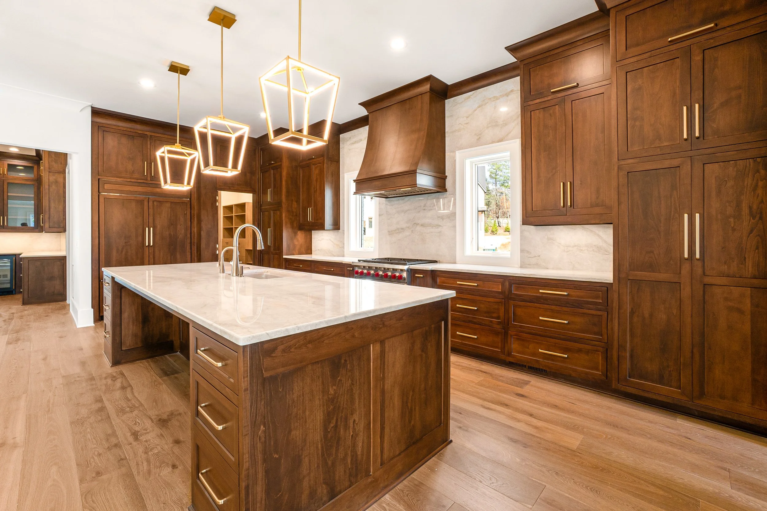 Modern kitchen with wooden cabinets, an island with a marble countertop, and pendant lights hanging from the ceiling.