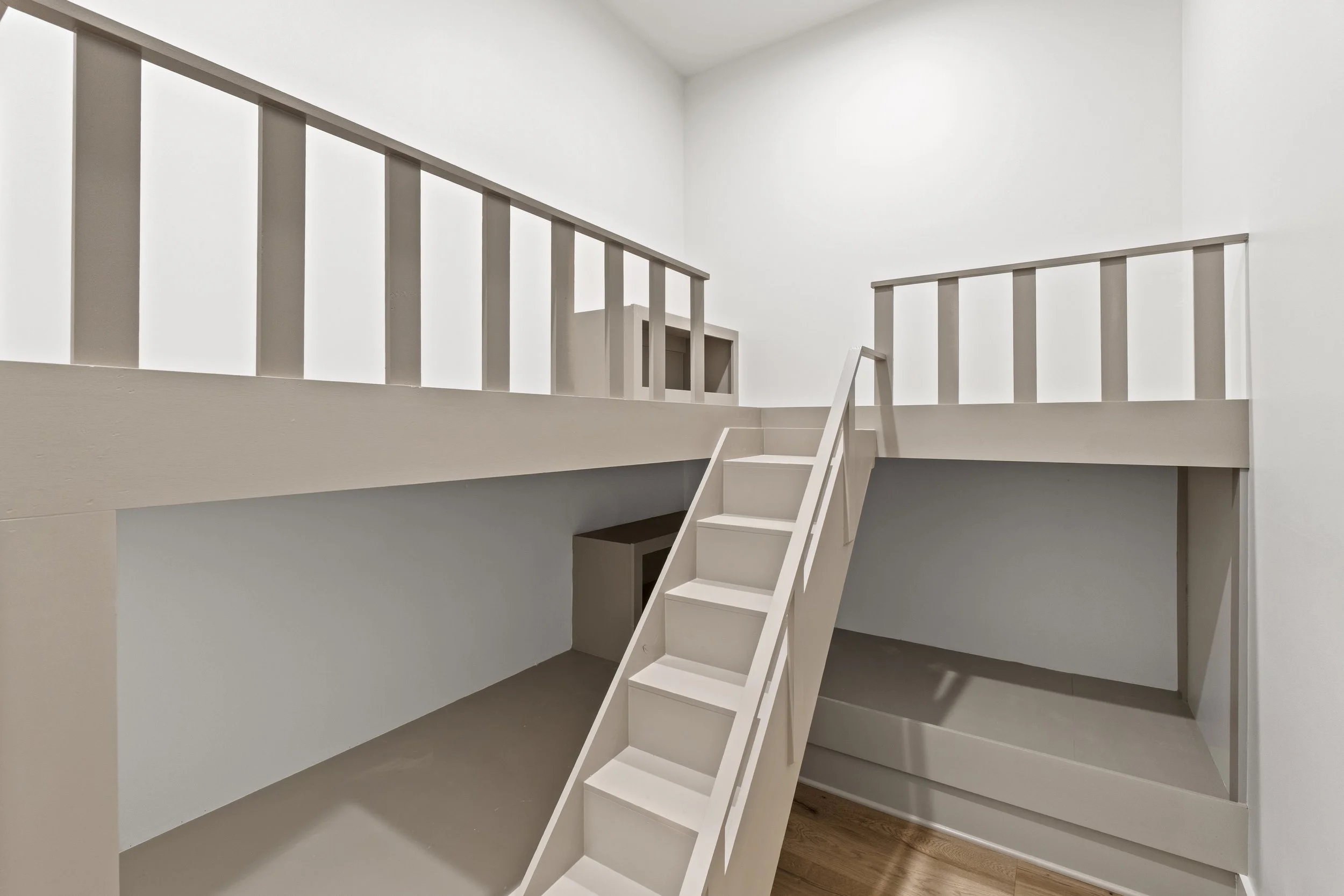 Empty white interior space with a staircase leading to a second level railing and a doorway, minimalistic design, with wooden flooring.