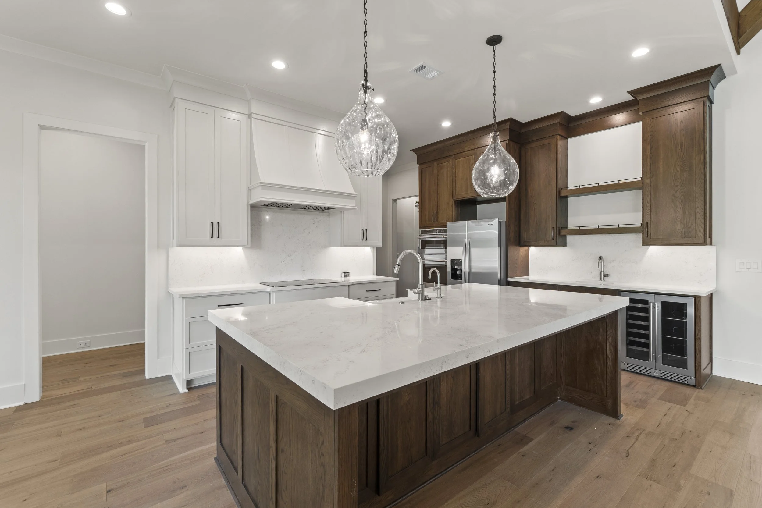 Modern kitchen with white and wooden cabinetry, a central island with a white marble countertop, two pendant lights, and stainless steel appliances.