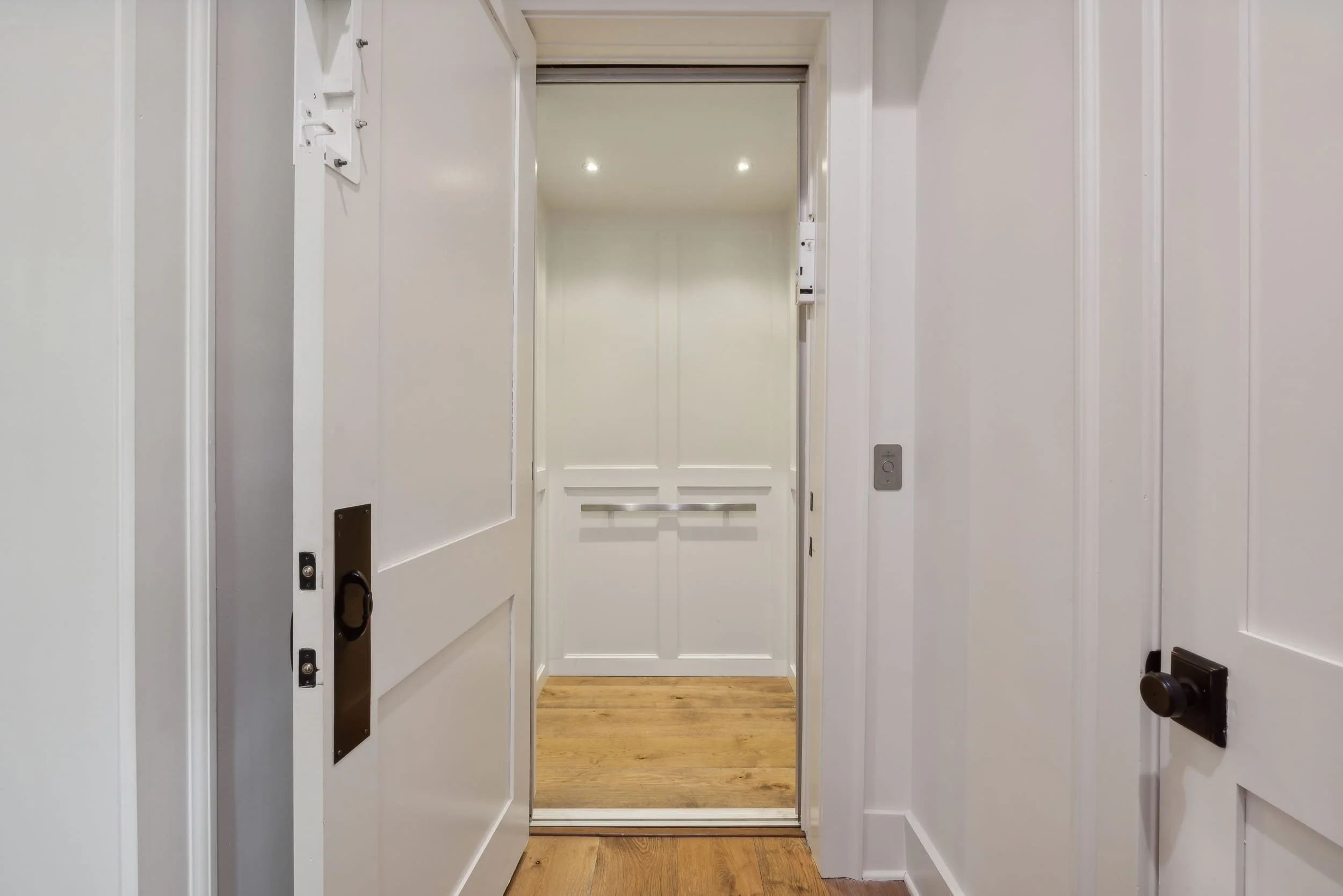 An elevator with open doors revealing a hallway with wooden flooring inside.